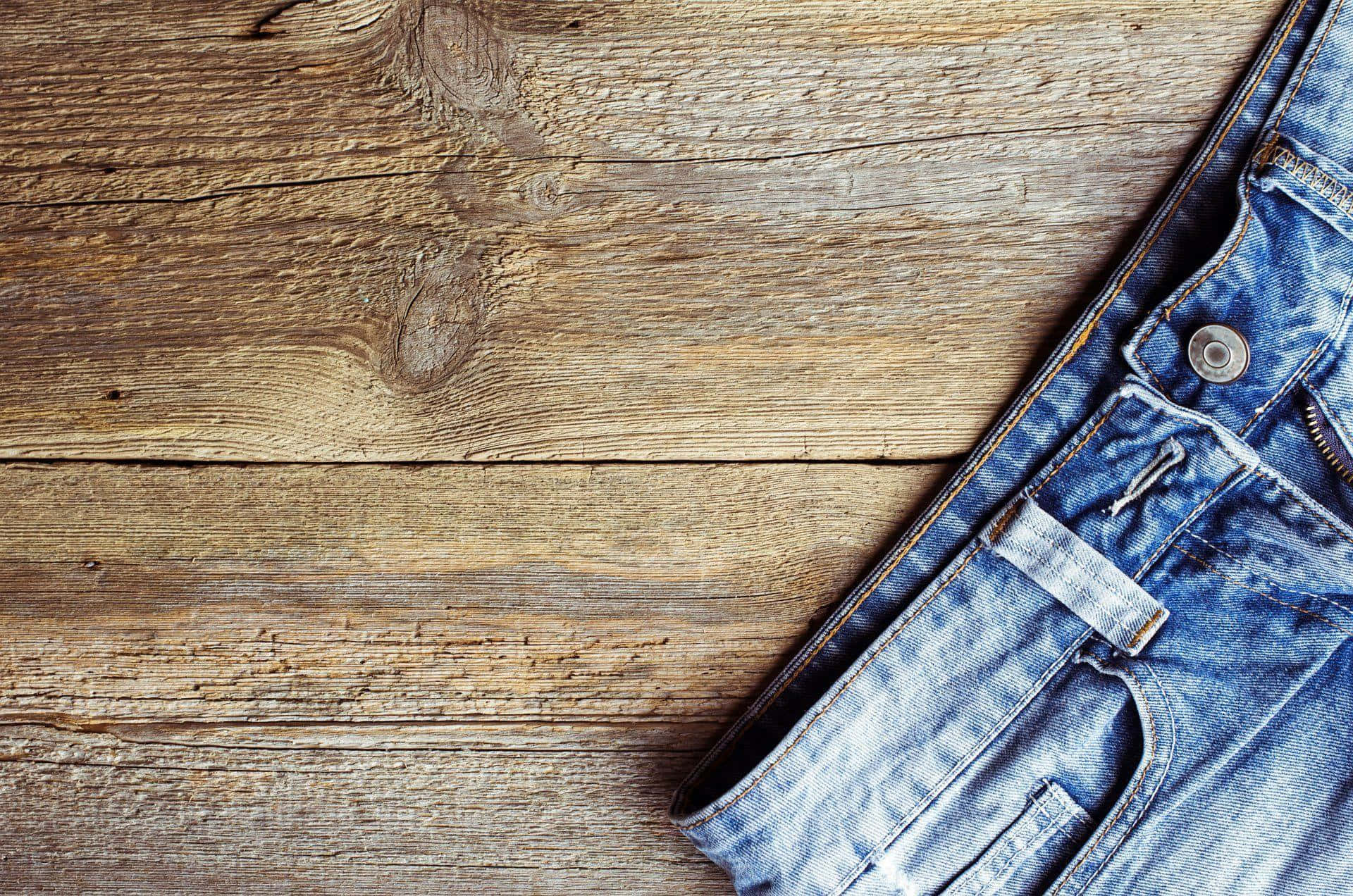 Jeans 桌布 壁紙 — 一條藍色牛仔褲斜放在一塊經風化的木質表面上，展現出天然的木紋和節疤。
