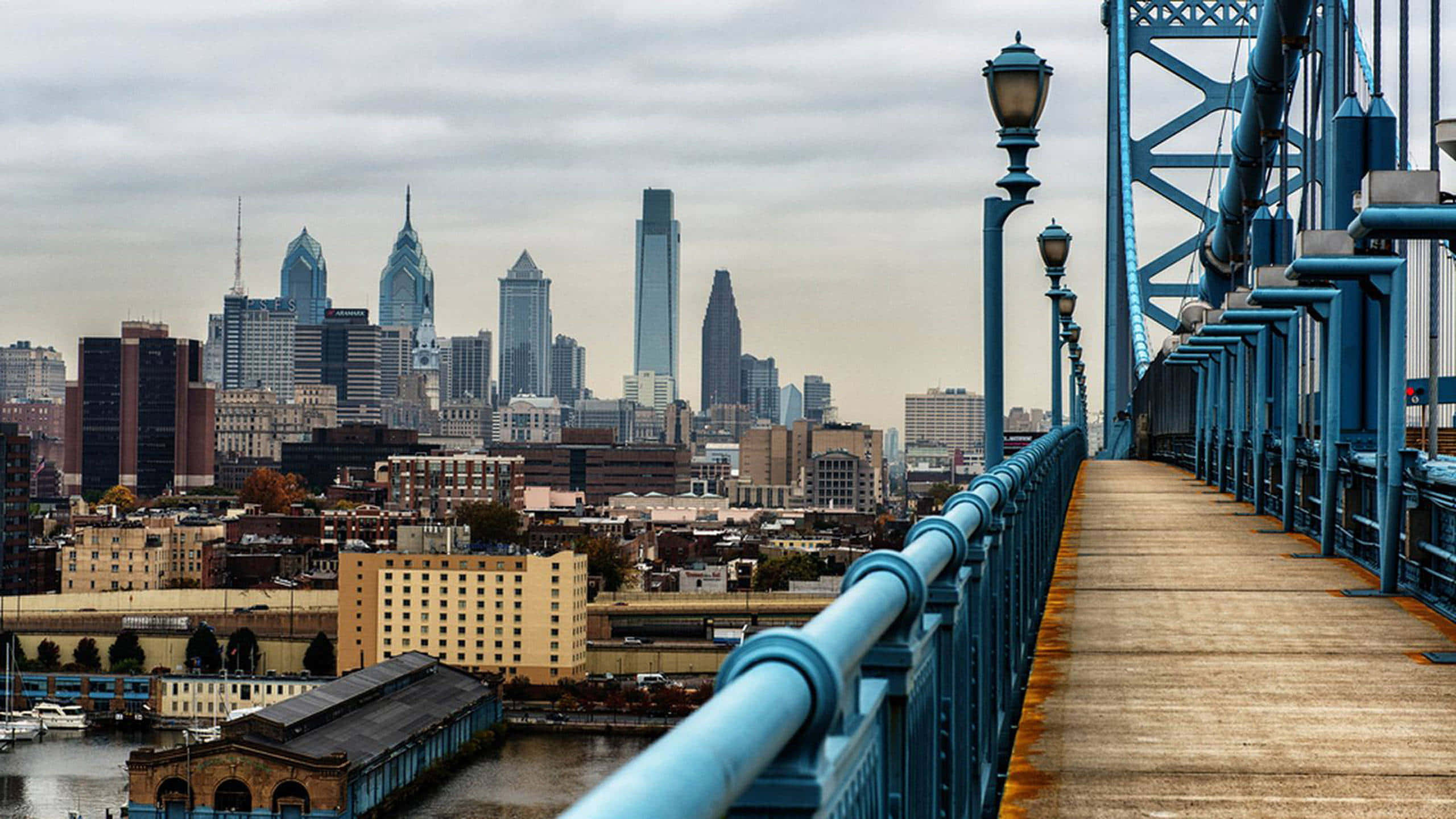 Philly 桌布 壁紙 — 一條藍色鋼橋通往多雲的城市天際線，高樓大廈和海濱建築。