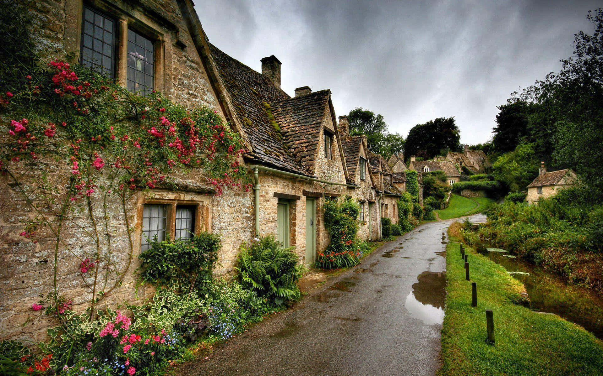 England 桌布 壁紙 — 一條蜿蜒潮濕的道路，在陰沉灰暗的天空下，蜿蜒經過裝飾著鮮豔粉紅色玫瑰的石屋。