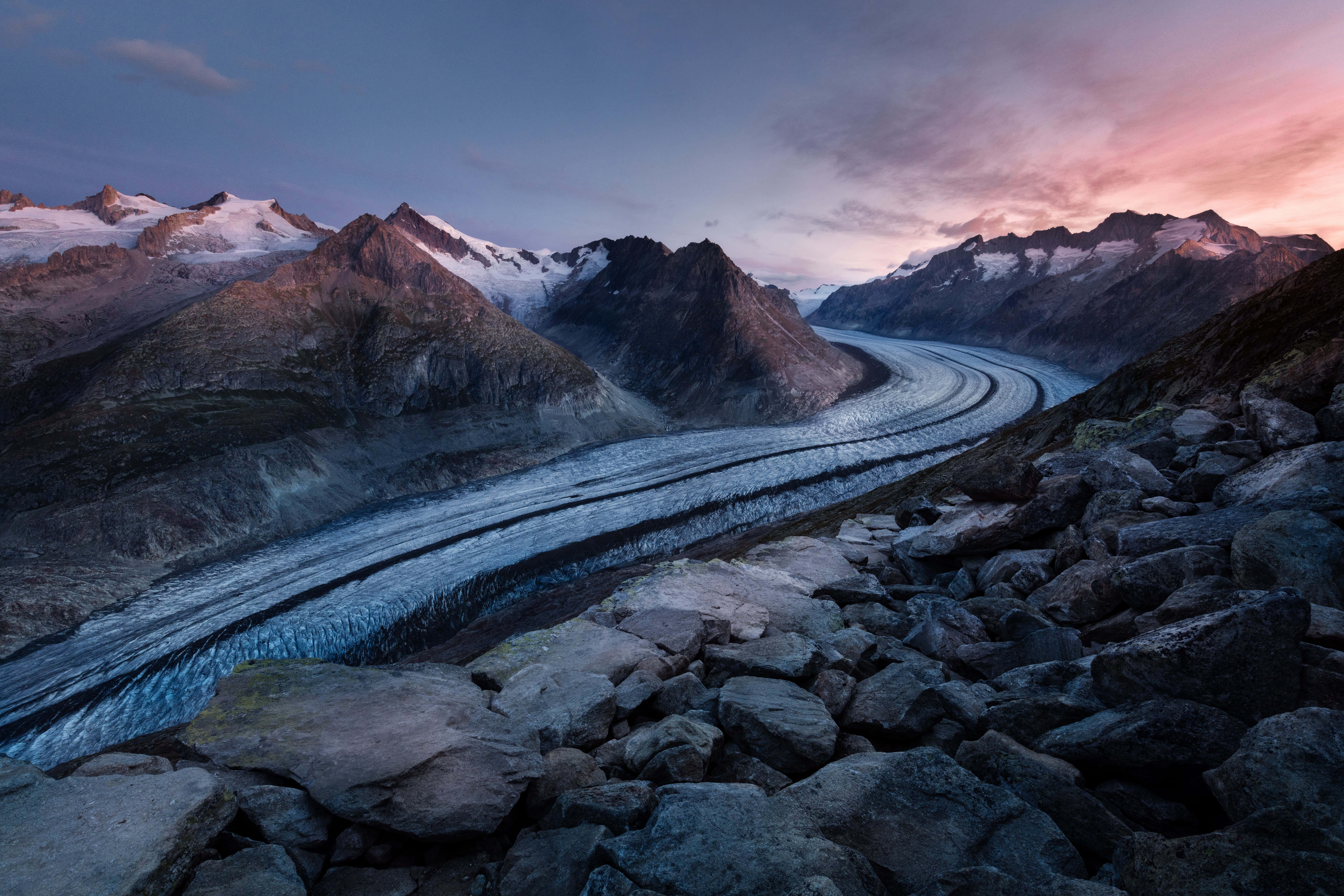 Photography Desktop 桌布 壁紙 — 一條蜿蜒的冰川在崎嶇的雪山之間蜿蜒而行，天空在暮色中染上粉紅和紫色調。