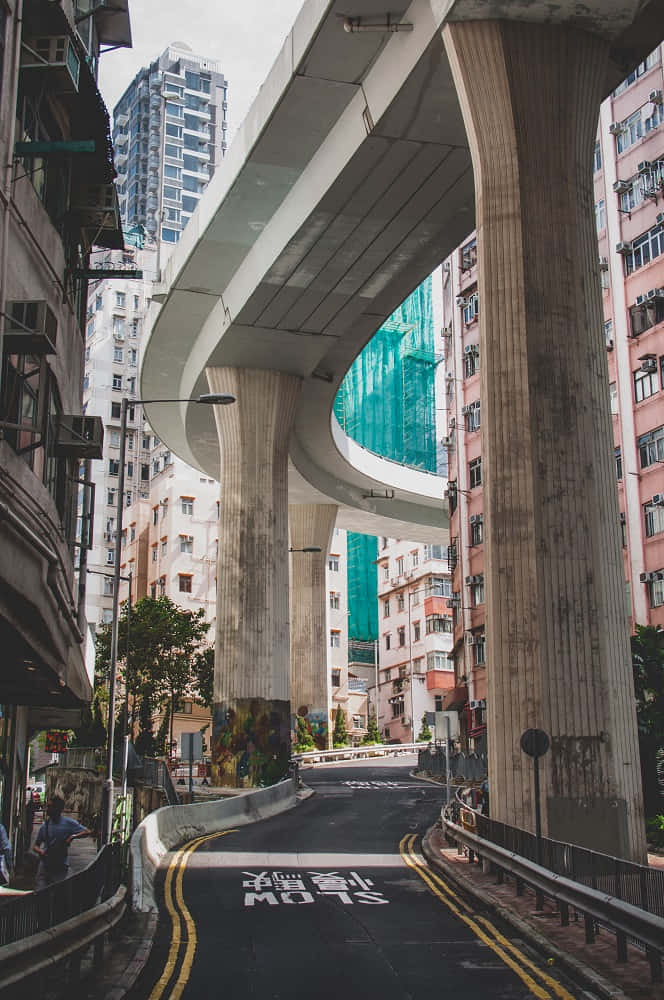 Soulful 桌布 壁紙 — 一條蜿蜒的城市街道在巨大的混凝土高架橋下彎曲，周圍是高聳的建築物和藍綠色玻璃外牆的密集城市景觀。