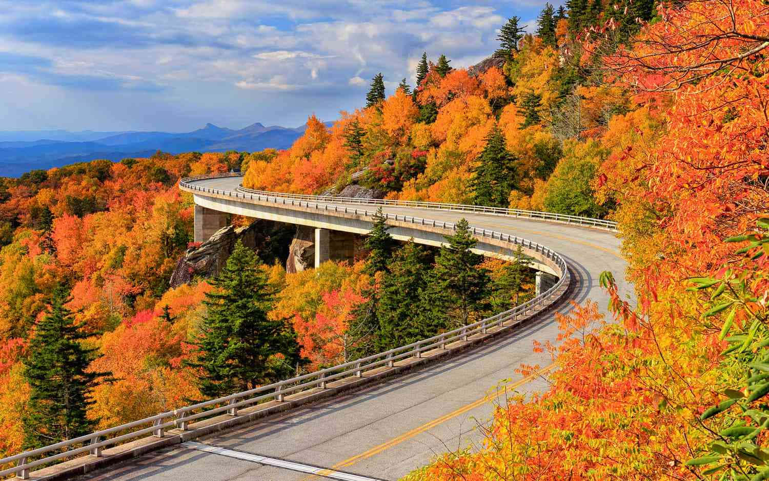 Autumn Fall 桌布 壁紙 — 一條蜿蜒的山路在部分多雲的天空下穿過充滿活力的秋葉。