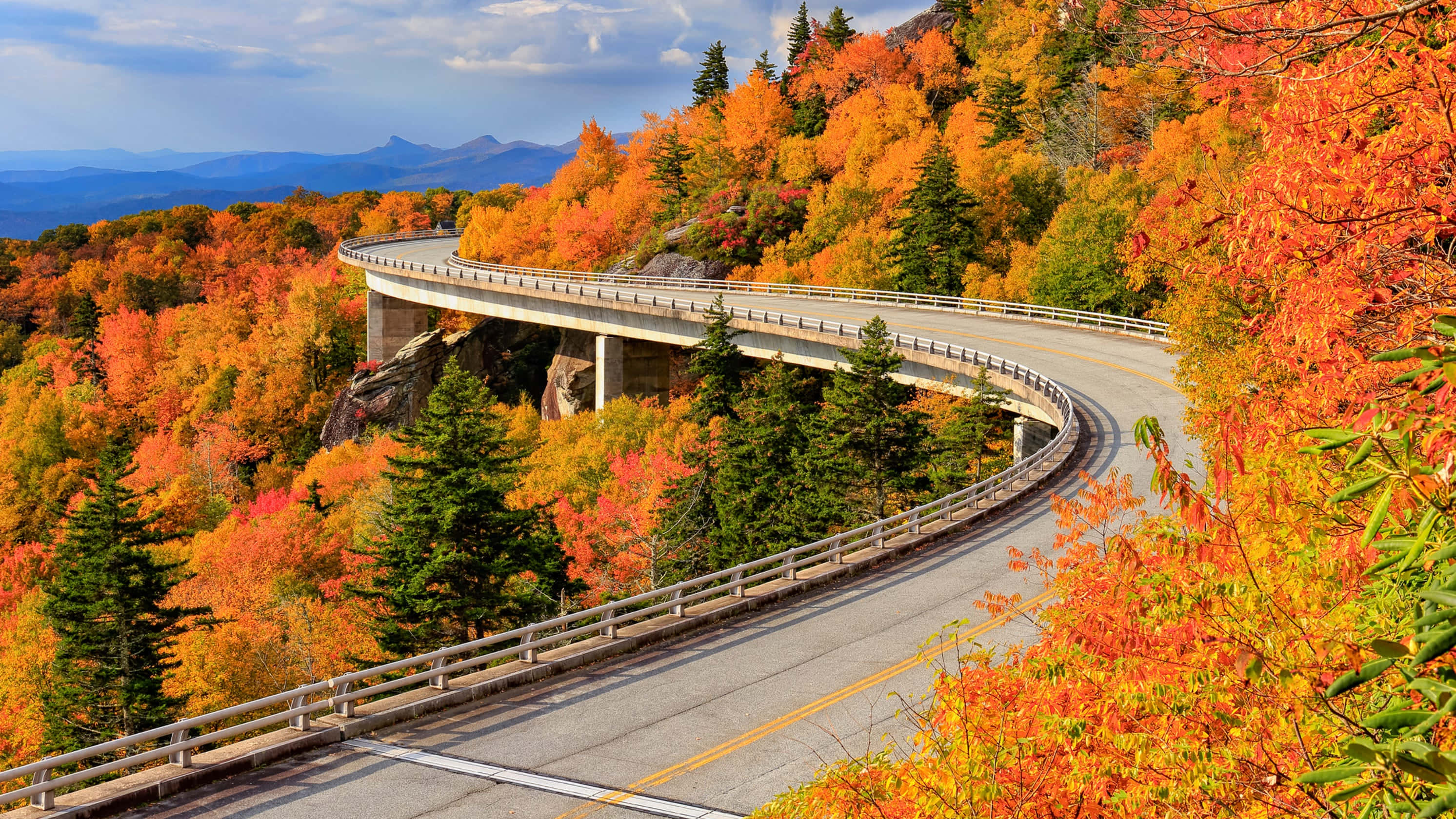 Blue Ridge Parkway 桌布 壁紙 — 一條蜿蜒的山路在部分多雲的天空下穿過充滿活力的秋葉。
