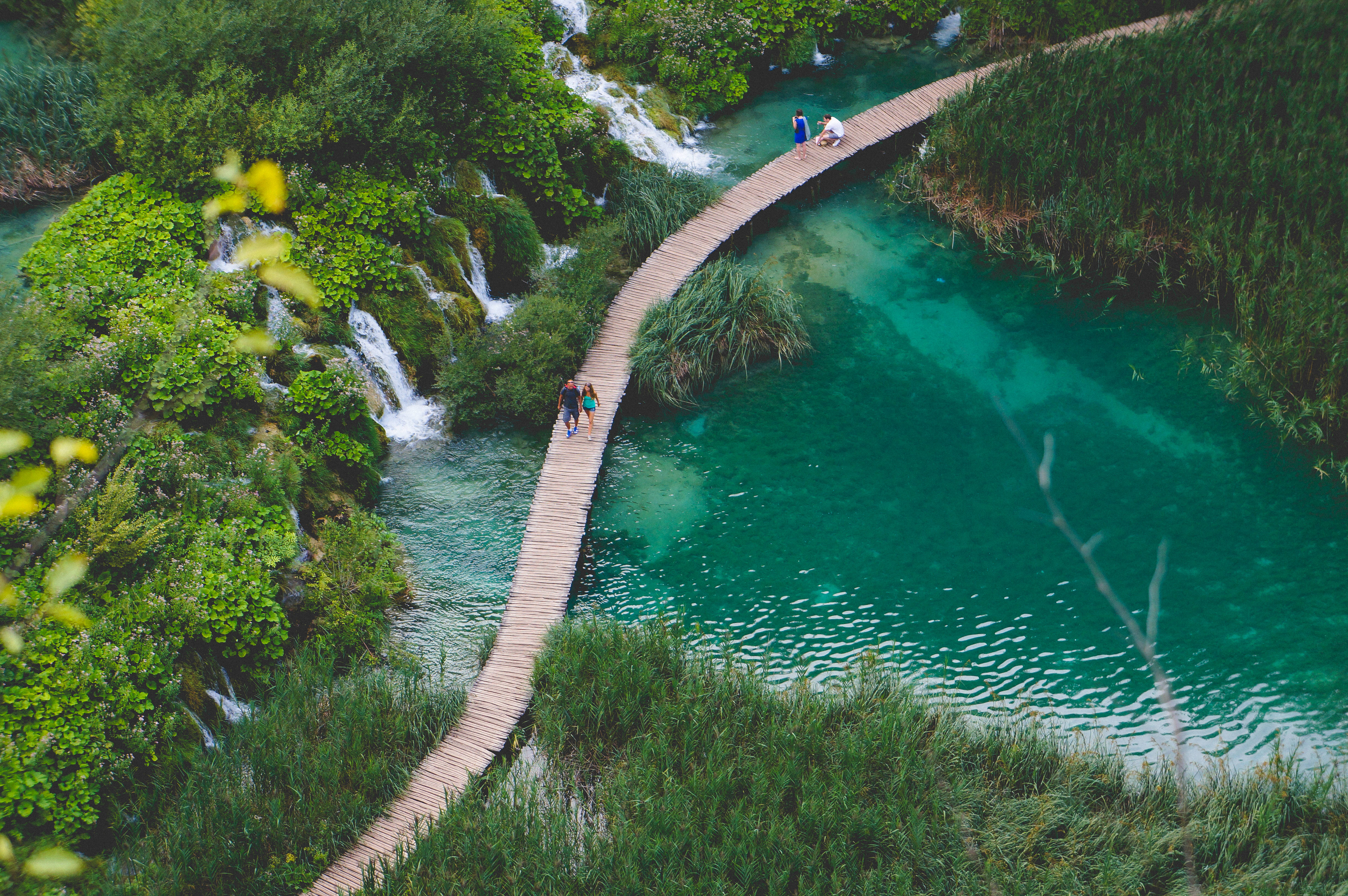 Croatia 桌布 壁紙 — 一條蜿蜒的木棧道穿過翠綠色的水域，瀑布層疊而下，茂密的綠植環繞著遊客。