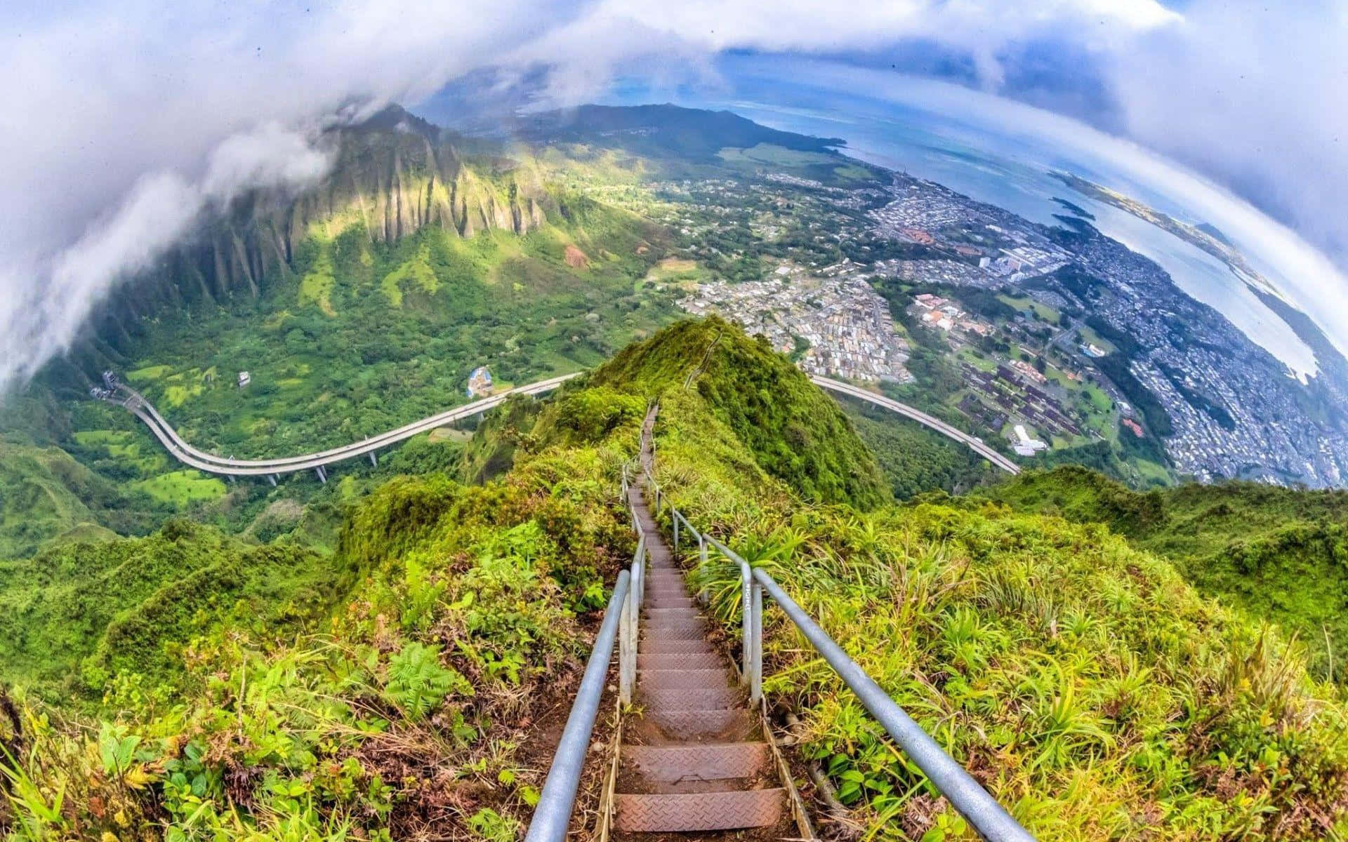 Stairway To Heaven 桌布 壁紙 — 一條蜿蜒的樓梯沿著翠綠的山脊向上延伸，俯瞰著雲天下的一個沿海小鎮和海洋。