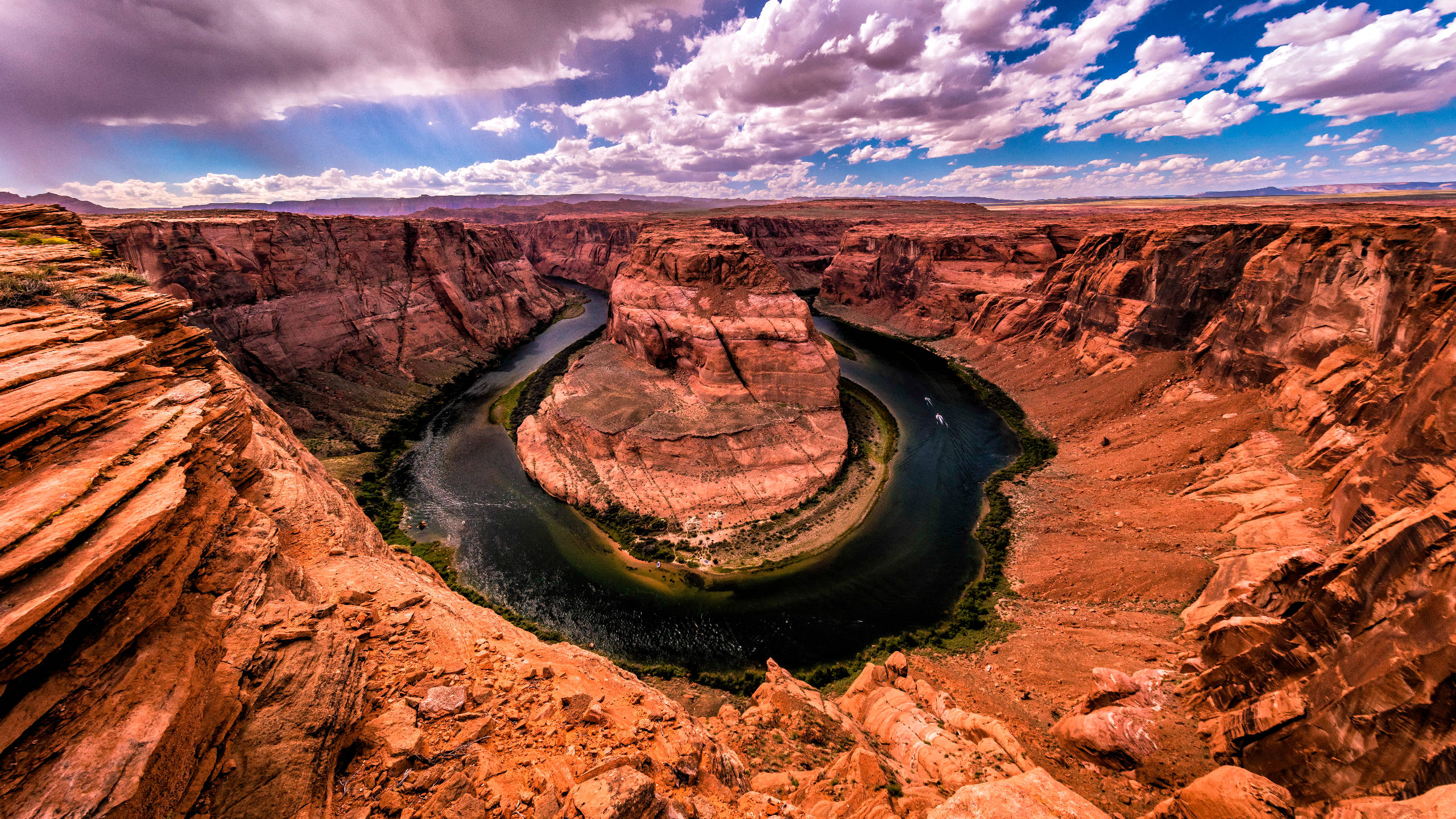 峽谷 桌布 壁紙 — 一條蜿蜒的河流在戲劇性的多雲天空下，在紅色岩石峽谷中雕刻出深深的馬蹄形彎曲。
