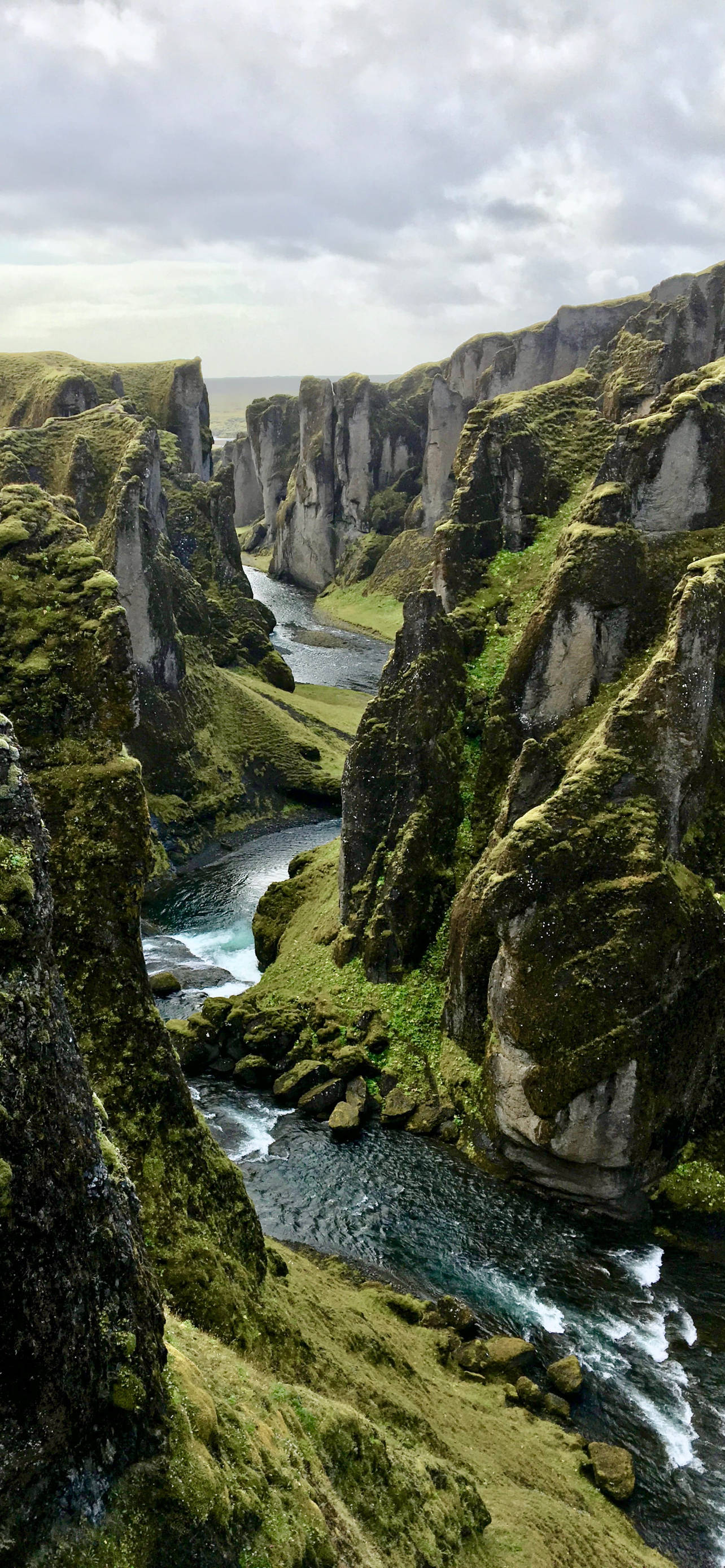 Canyon 桌布 壁紙 — 一條蜿蜒的河流在陰天之下，穿過一個長滿苔蘚的壯觀峽谷。