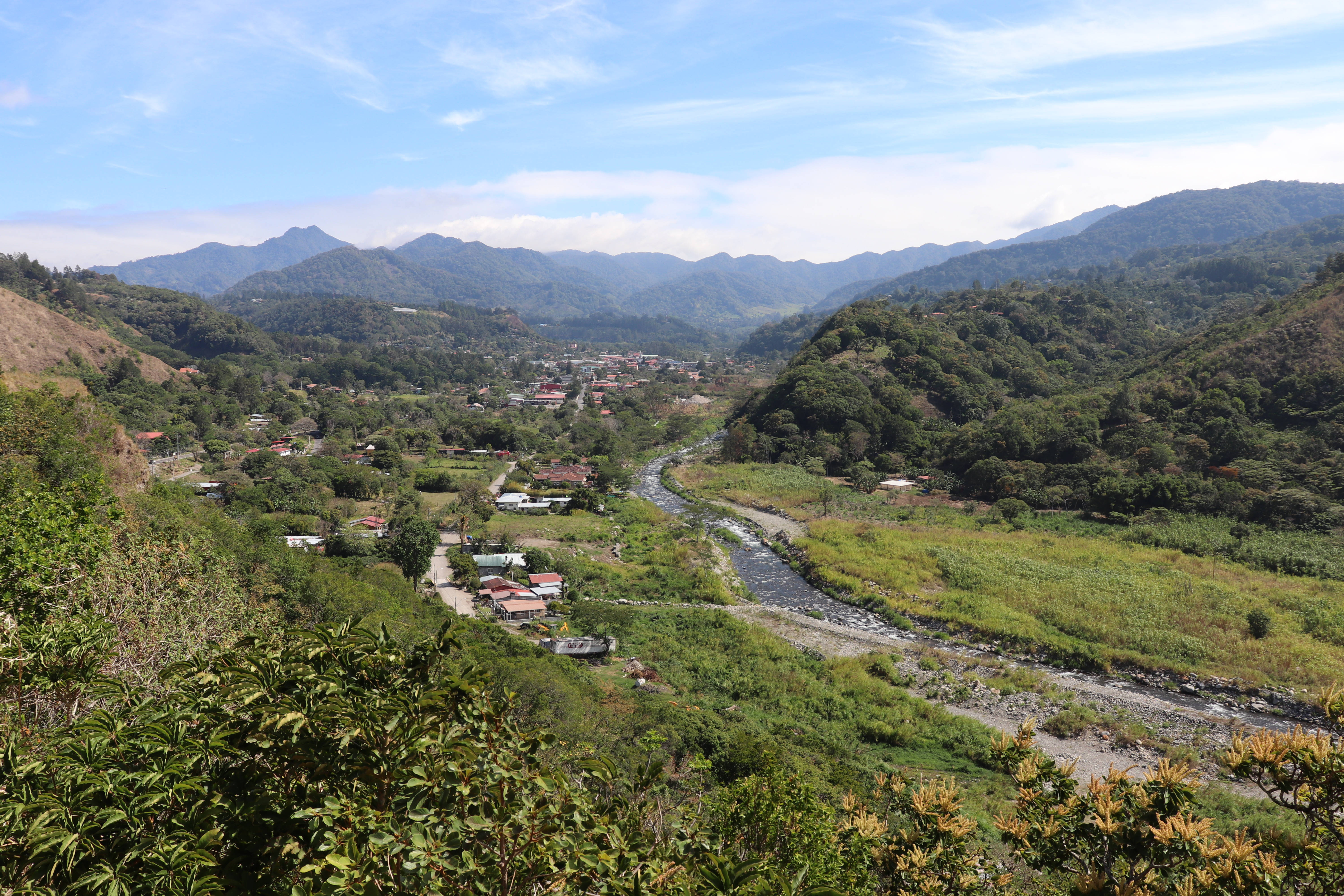Panama 桌布 壁紙 — 一條蜿蜒的河流流經鬱鬱蔥蔥的綠色山谷，散落的房屋坐落在連綿起伏的丘陵之間，上方是明亮的藍天。