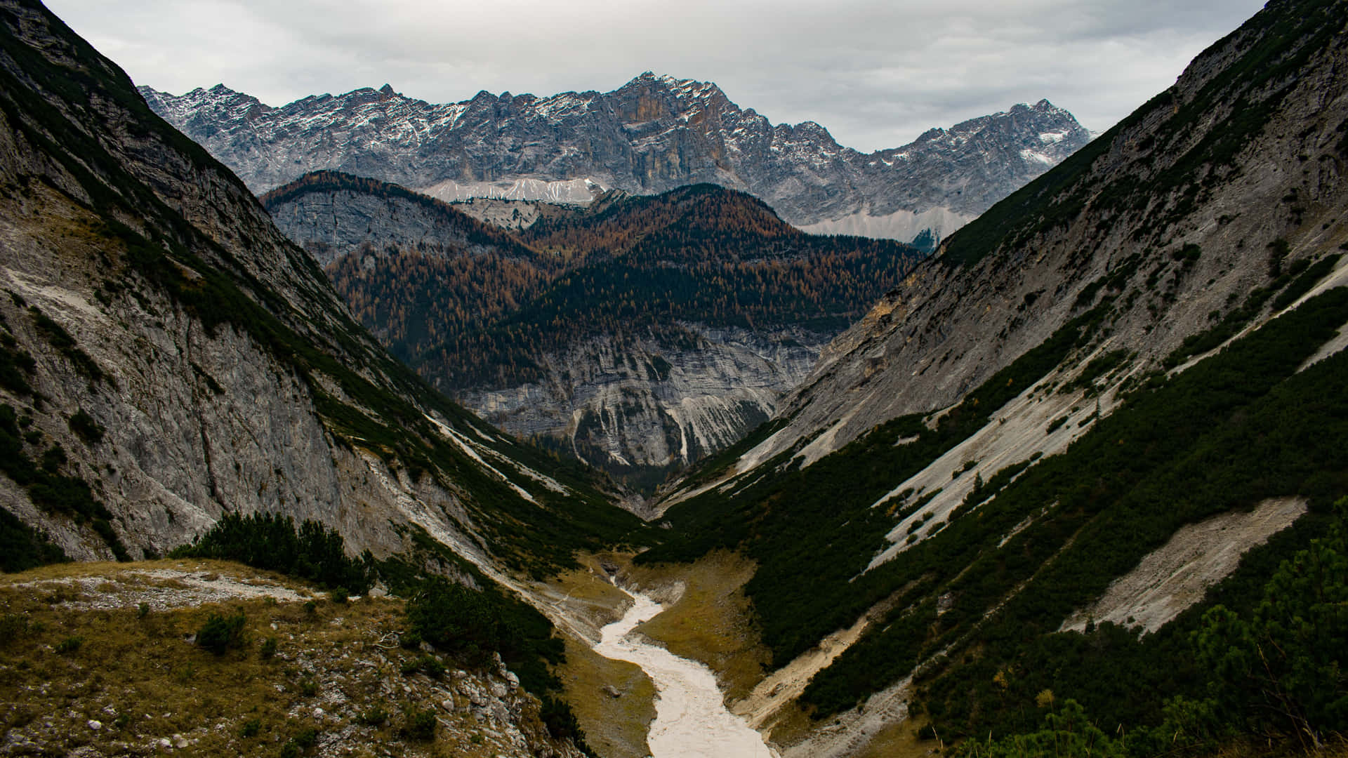 一條河流流經山谷，遠處有白雪覆蓋的山峰。 — 5K 壁紙