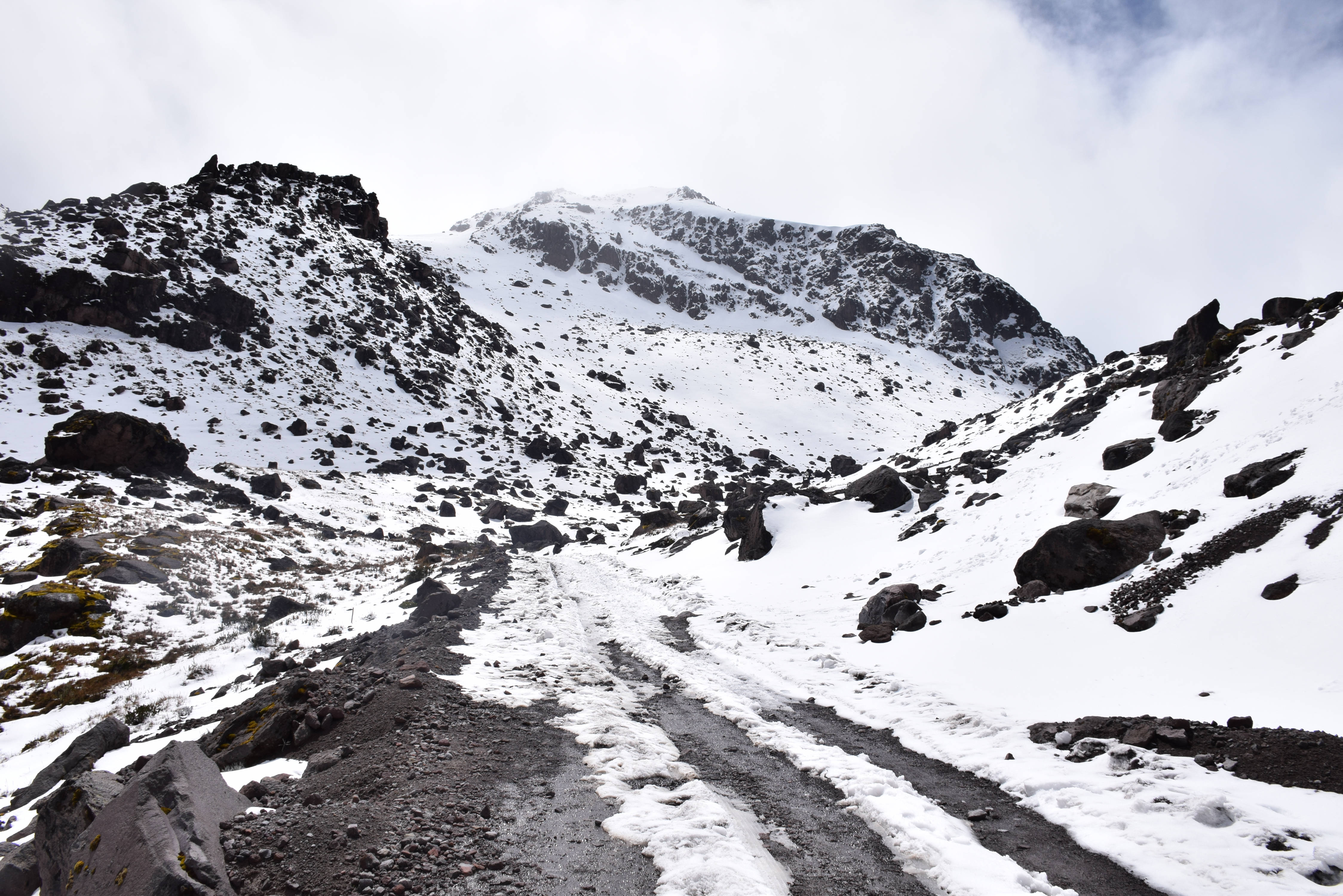 Ecuador 桌布 壁紙 — 一條蜿蜒的泥土小徑穿過被薄雪覆蓋的岩石山脈，天空多雲。