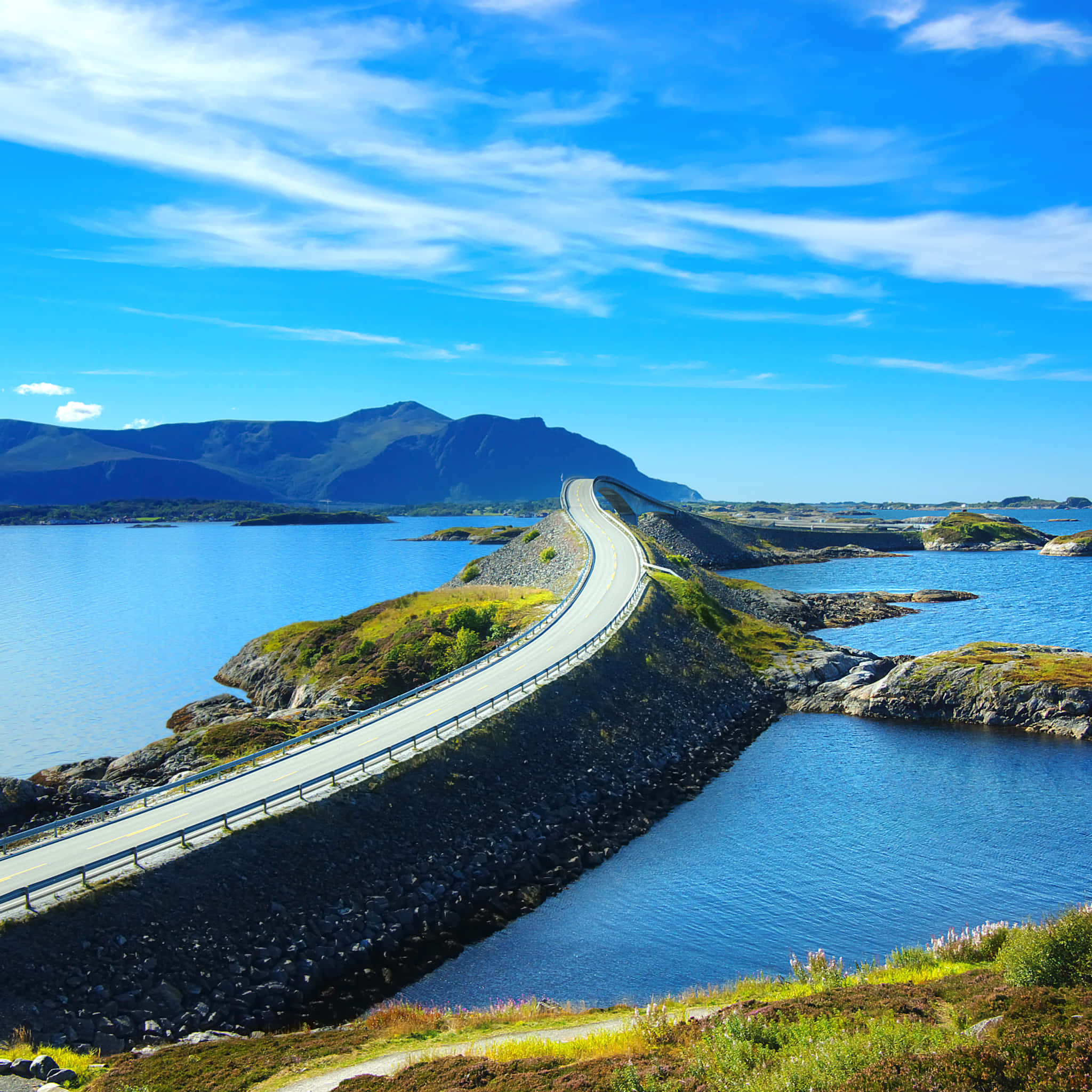 Road 桌布 壁紙 — 一條蜿蜒的海岸公路在岩石島嶼間穿梭，上方是藍天白雲。
