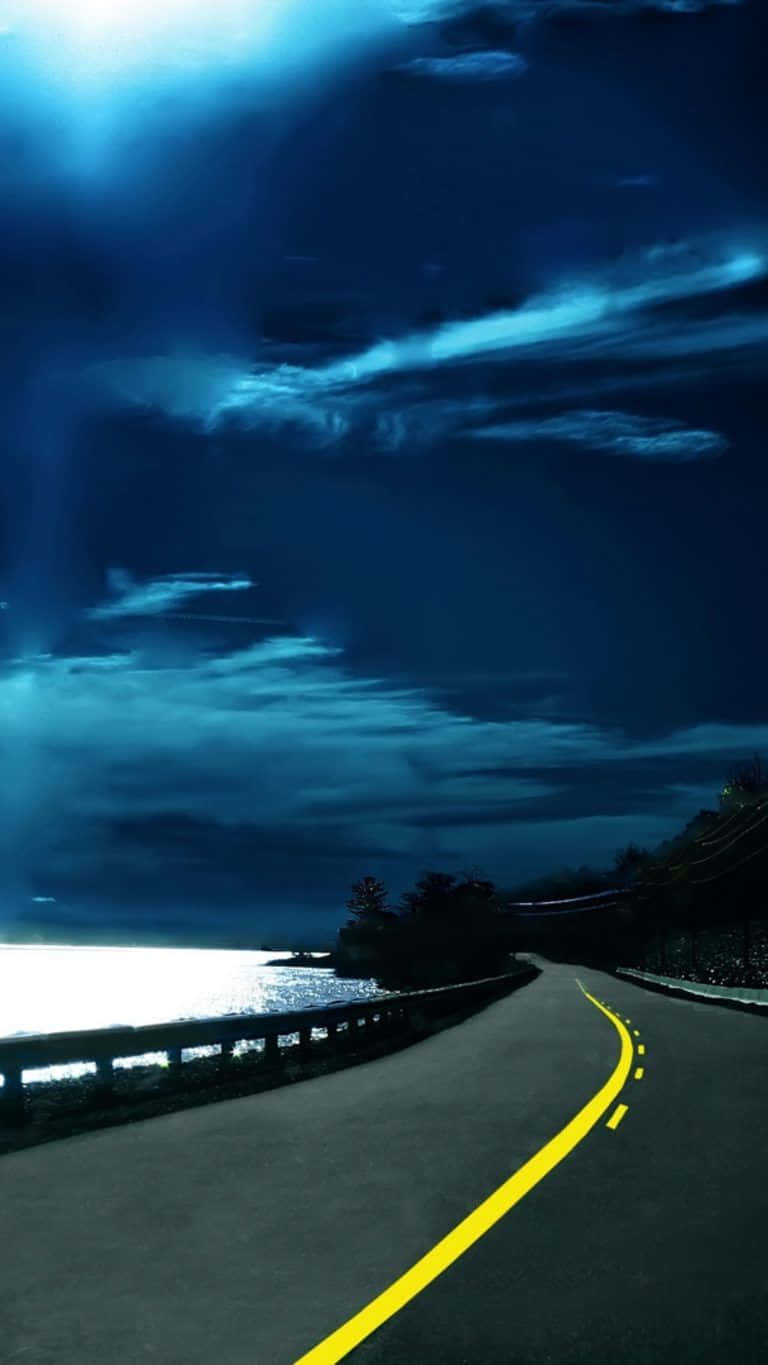 Path 桌布 壁紙 — 一條蜿蜒的海岸公路在戲劇性的夜空下彎曲，夜空中有發光的雲朵和一條明亮的黃線指引方向。