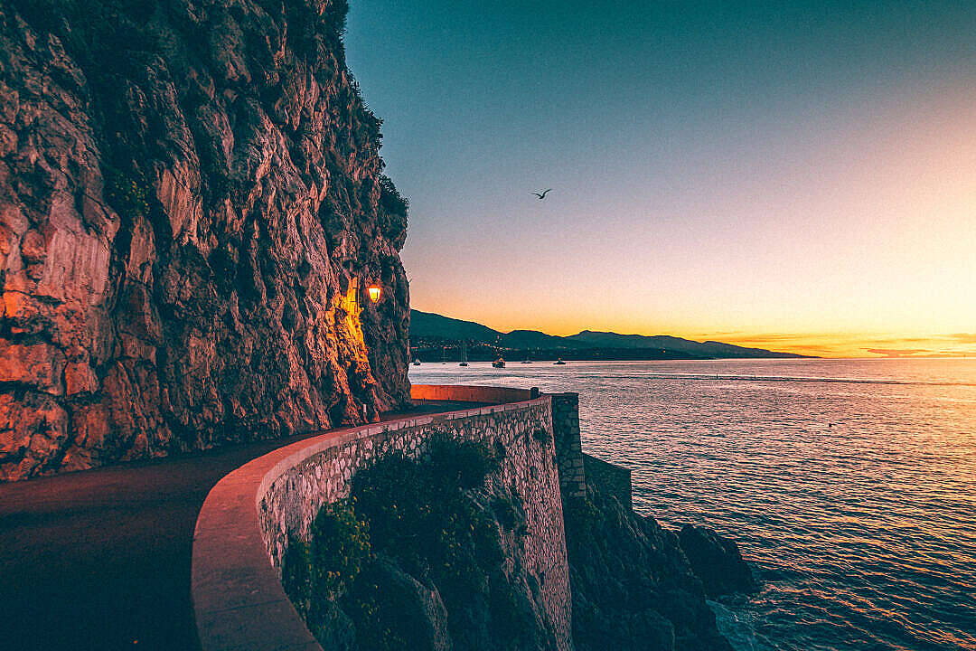 Sunrise Nature 桌布 壁紙 — 一條蜿蜒的海岸公路在日落時分緊貼懸崖，溫暖的燈光在清涼的藍色和橙色天空中閃耀。