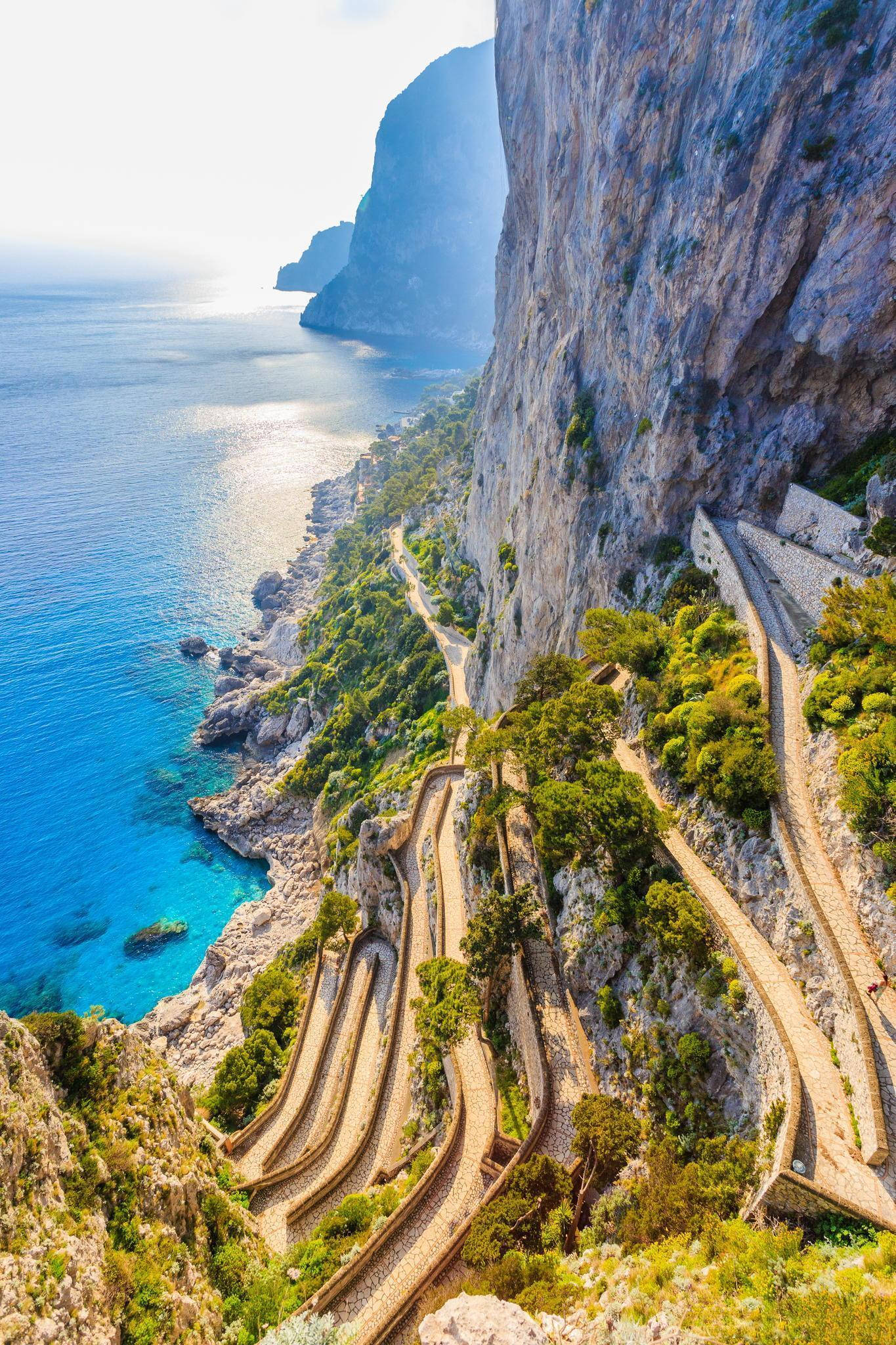 Capri 桌布 壁紙 — 一條蜿蜒的海岸公路在明亮的日光下緊貼著陡峭的懸崖，下方是碧綠的海水。