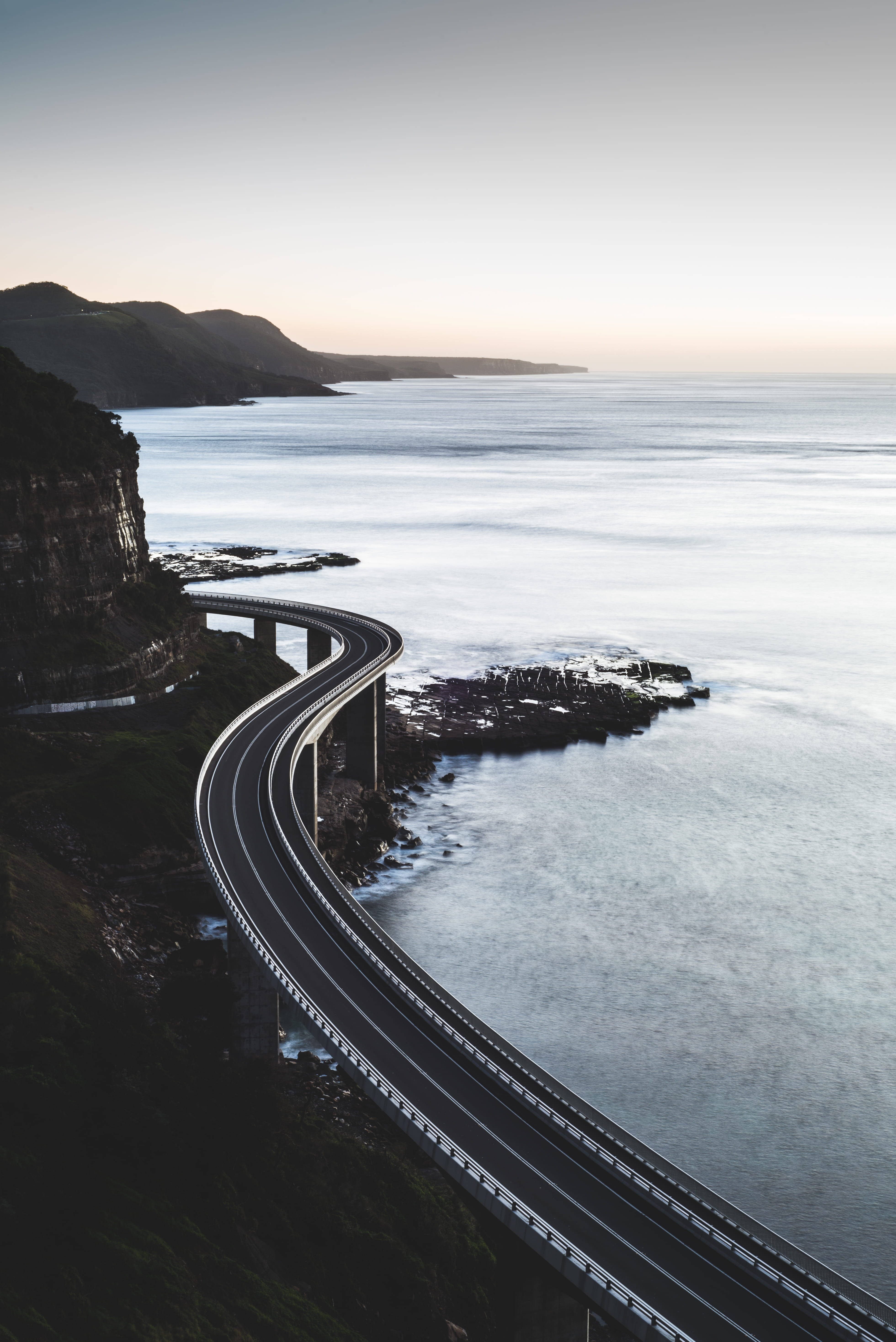 Road 桌布 壁紙 — 一條蜿蜒的海岸高速公路沿著懸崖蜿蜒而行，俯瞰著金色時刻平靜的海水。