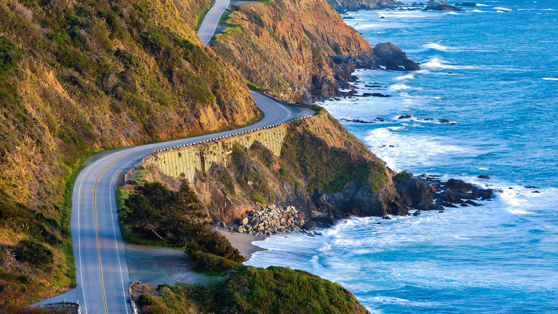 Seaside 桌布 壁紙 — 一條蜿蜒的海岸高速公路緊貼陡峭的懸崖，俯瞰著碧綠的海浪拍打岩石海岸。