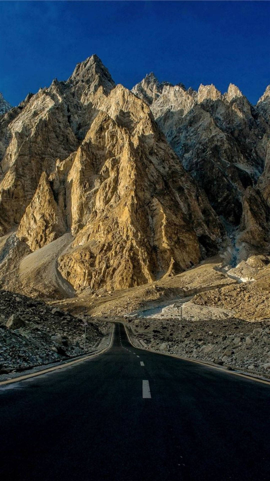 Pakistan 桌布 壁紙 — 一條蜿蜒的瀝青公路穿過高聳的金棕色山峰，在深藍色的天空下。
