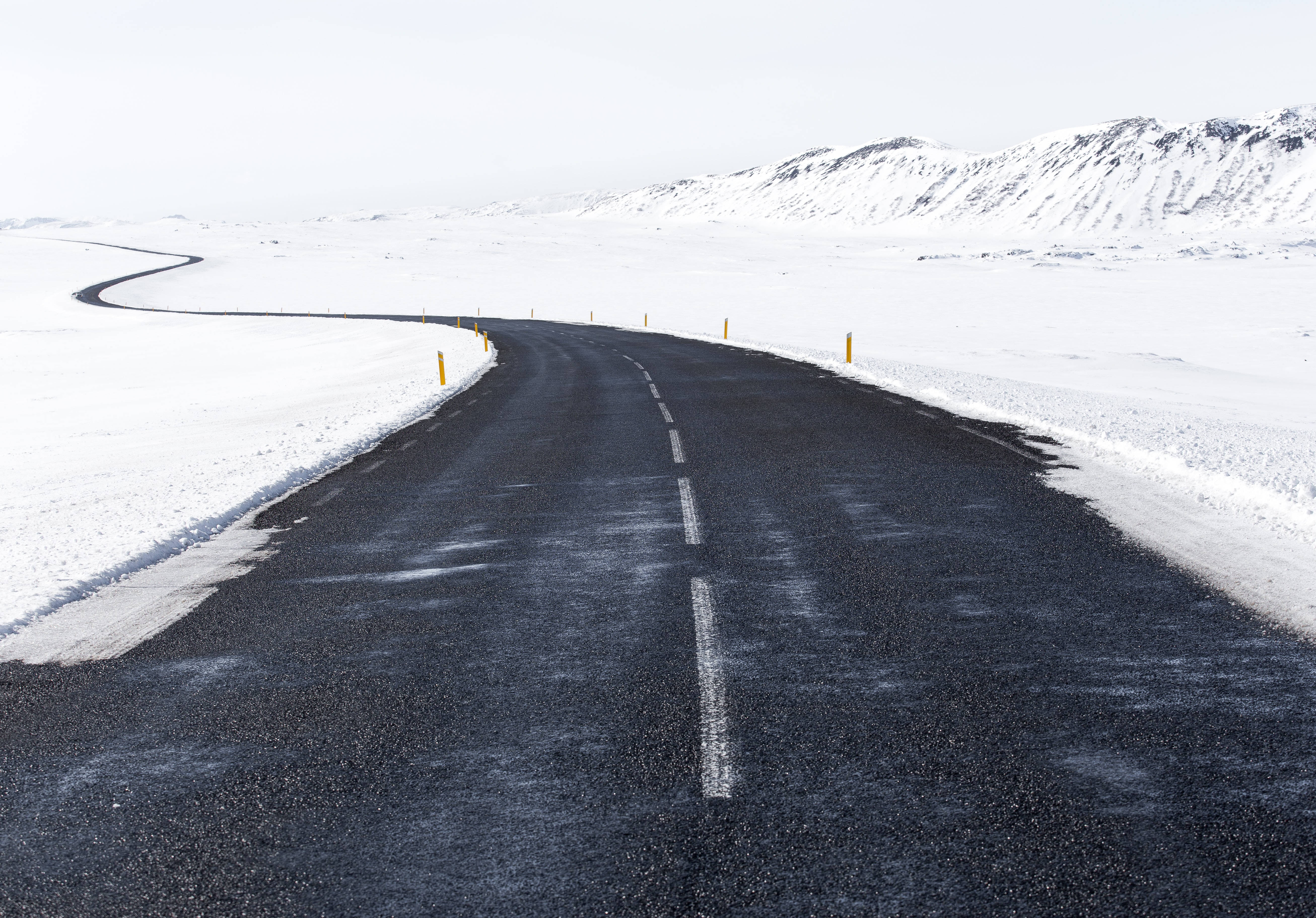 Tumblr 桌面版 桌布 壁紙 — 一條蜿蜒的瀝青路穿過廣闊的雪景，遠處有白雪覆蓋的山脈，天空蒼白。