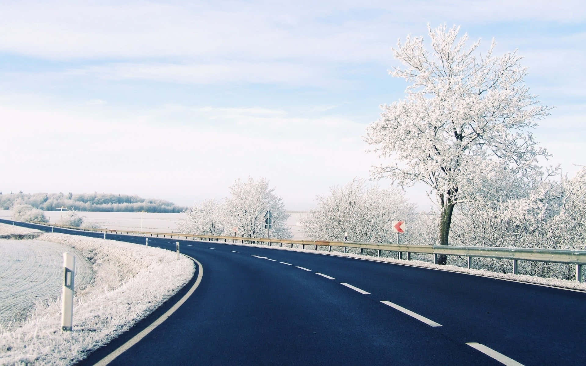 Road 桌布 壁紙 — 一條蜿蜒的瀝青路穿過結霜的冬季景觀，兩旁是白雪覆蓋的樹木和淡藍色的天空。