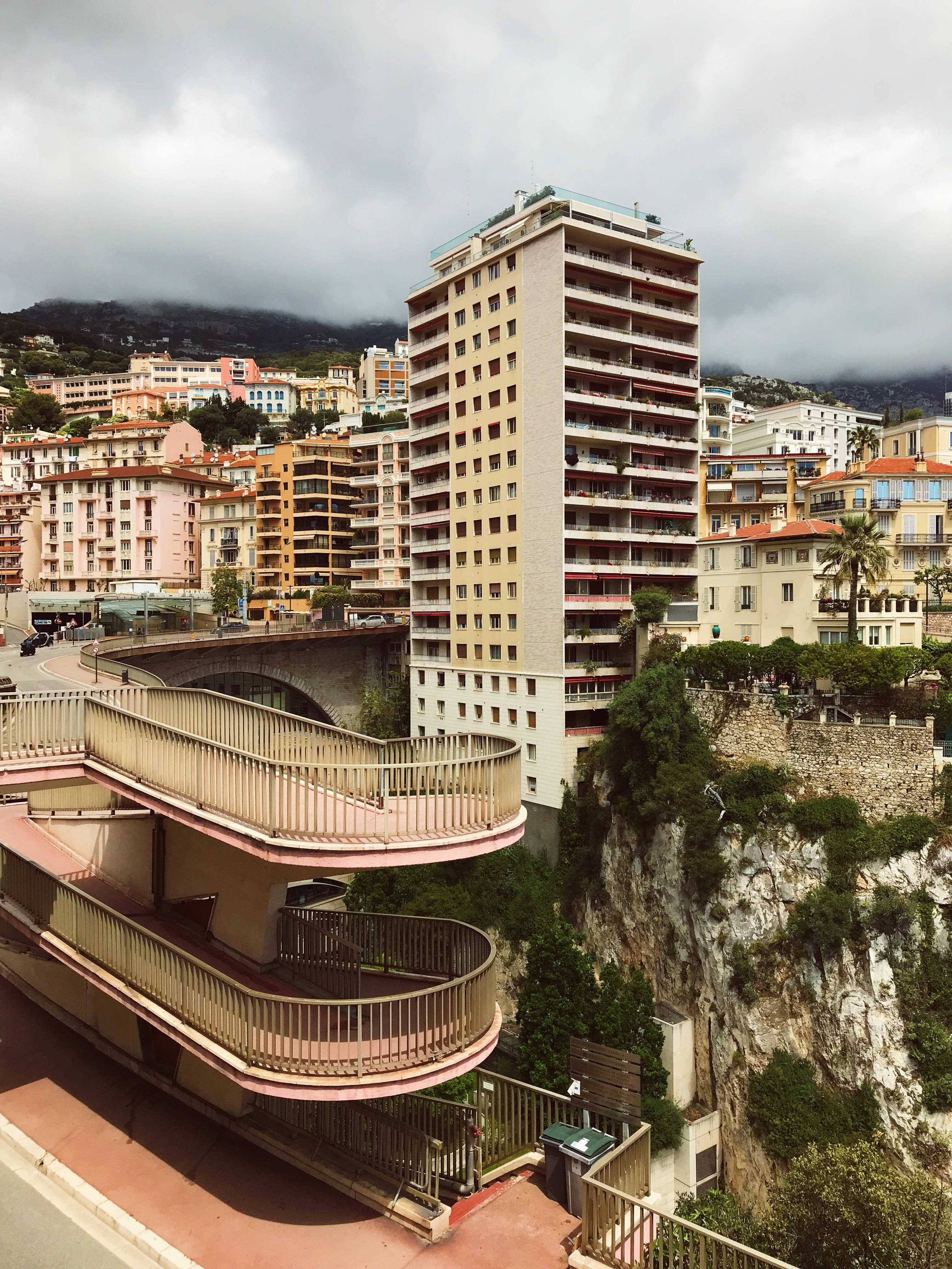 Monaco 桌布 壁紙 — 一條蜿蜒的行人天橋在陰天之下優雅地彎曲，橫跨懸崖邊的城市景觀。