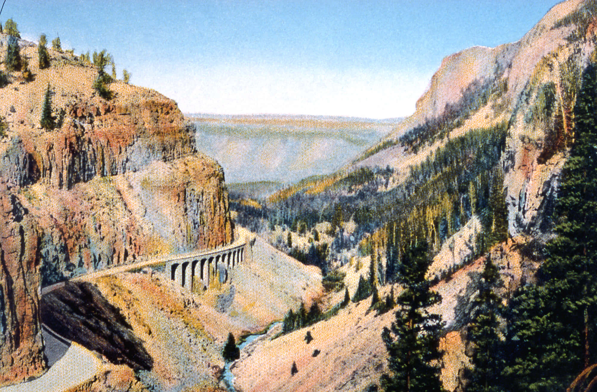 Yellowstone 桌布 壁紙 — 一條蜿蜒的道路和石橋穿越深峽谷，兩旁是崎嶇的懸崖和常綠森林，在清澈的藍天下。
