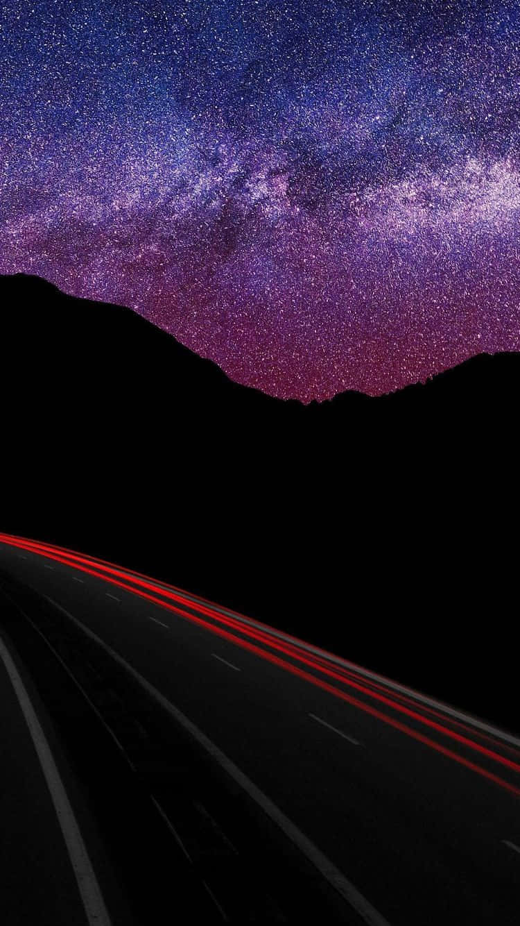 iPhone Home Screen 桌布 壁紙 — 一條蜿蜒的道路在夜晚彎曲，下方是充滿活力的紫色和藍色星空，銀河在頭頂拱起。