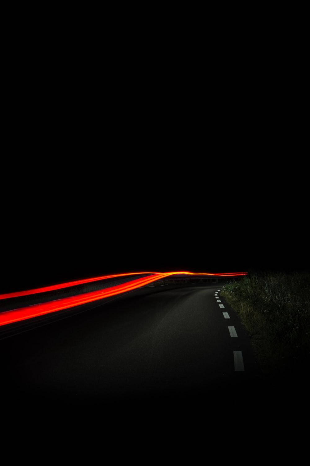 手機 桌布 壁紙 — 一條蜿蜒的道路在夜晚被移動車輛的鮮紅色光軌照亮，背景是漆黑的天空。