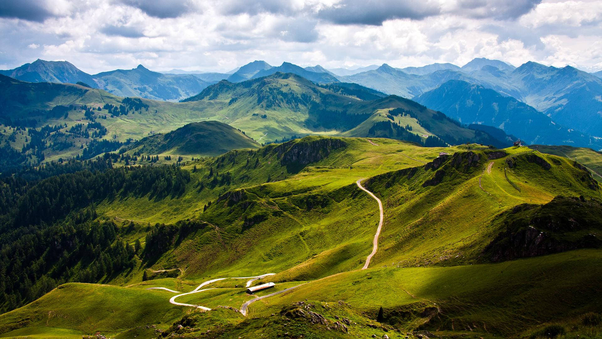 Beautiful Mountain View 桌布 壁紙 — 一條蜿蜒的道路在戲劇性的多雲天空下蜿蜒穿過充滿活力的綠色山谷。