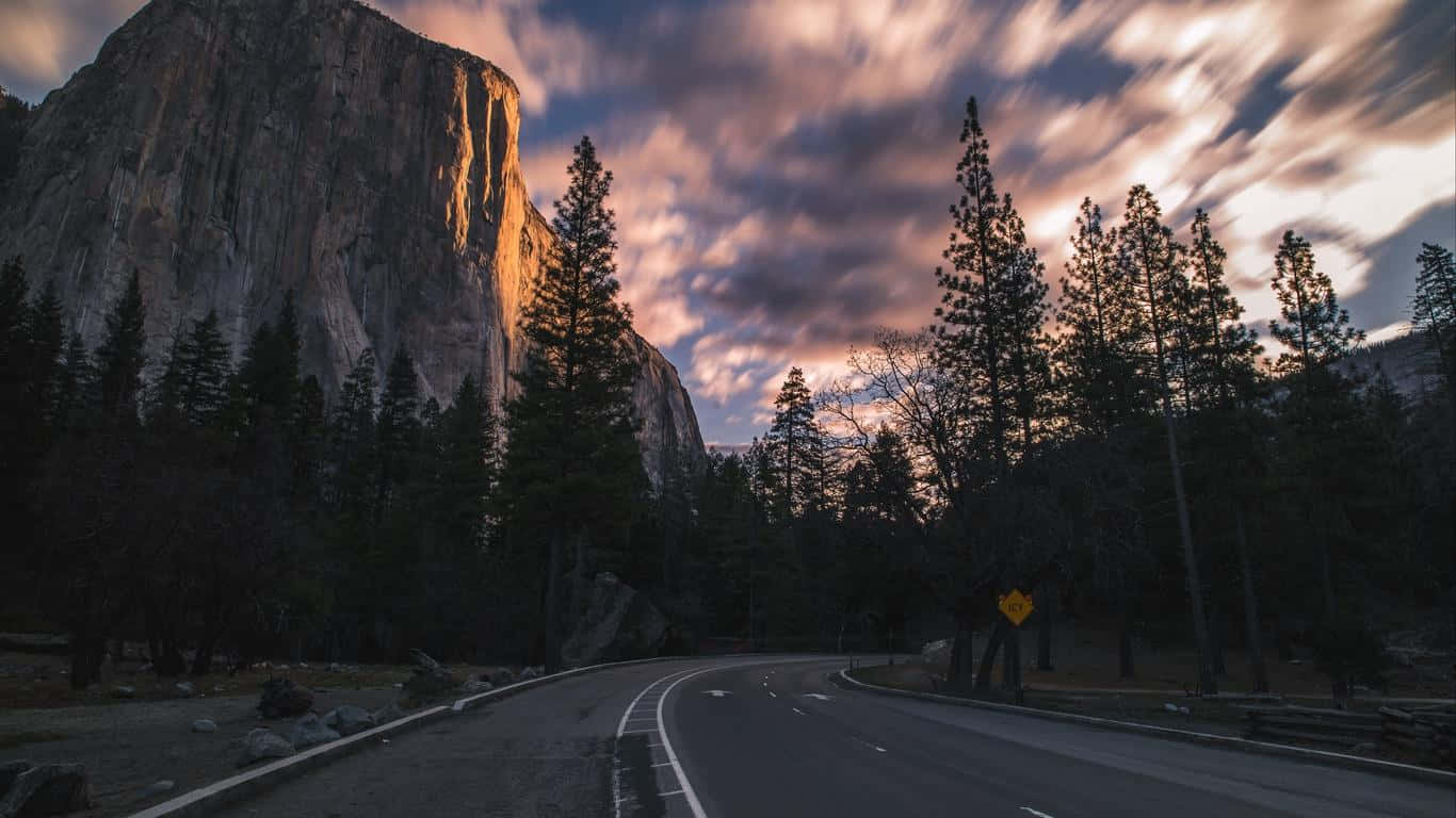 自然 桌布 壁紙 — 一條蜿蜒的道路在日落時分穿過森林，巨大的花崗岩懸崖被金色的光芒照亮。