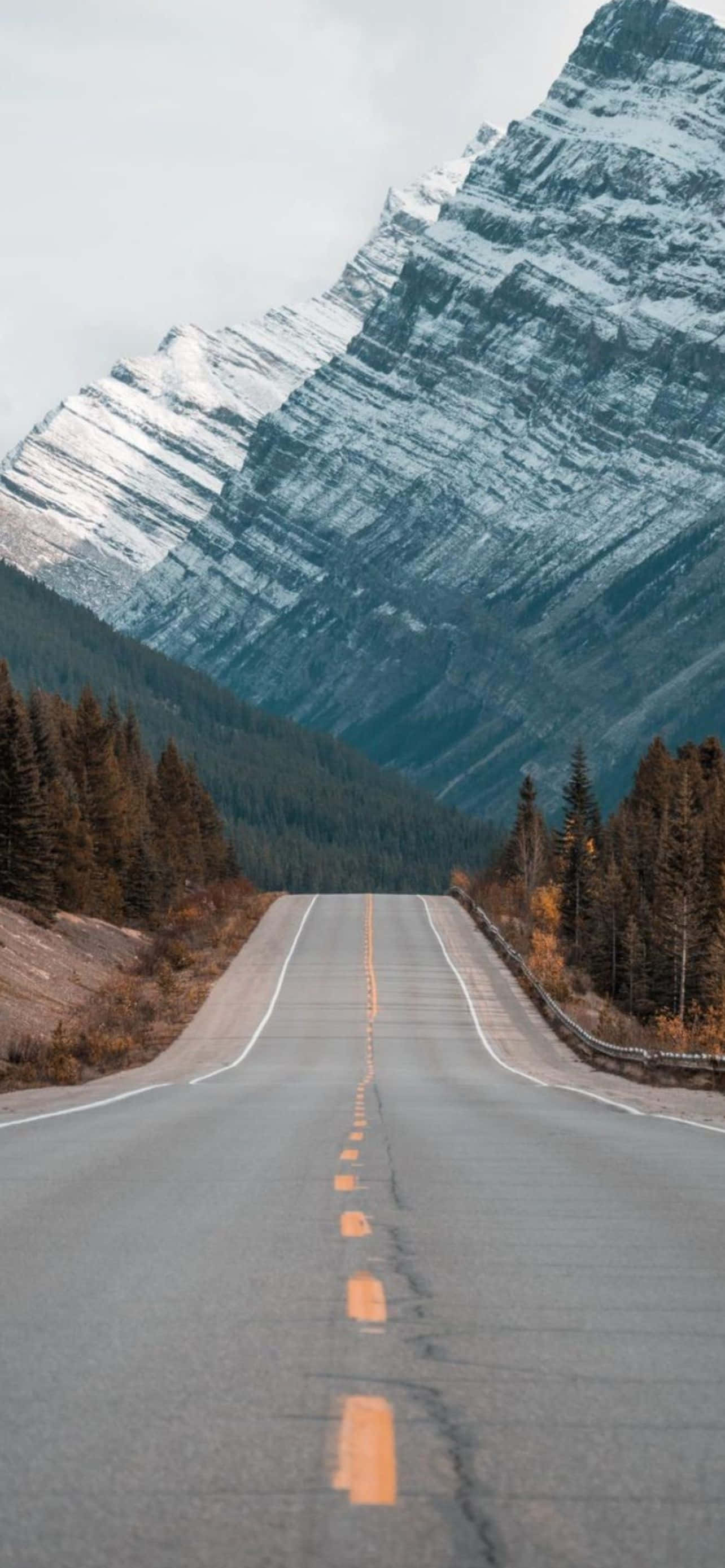 Mountain iPhone 桌布 壁紙 — 一條蜿蜒的道路在陰天延伸向一座高聳的雪山。
