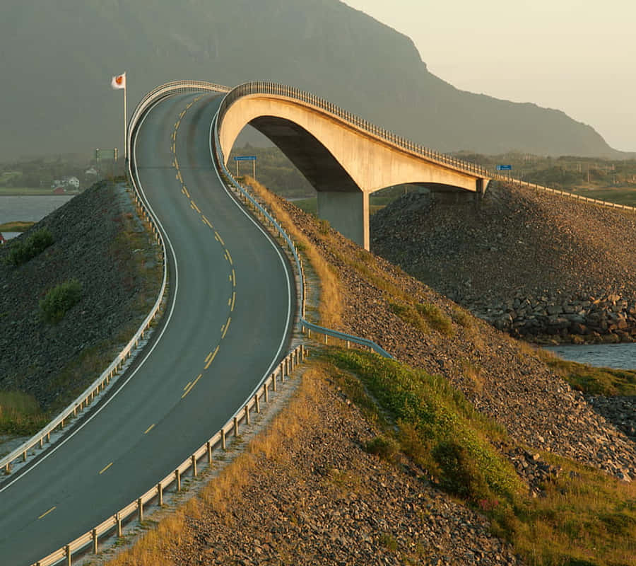 Road 桌布 壁紙 — 一條蜿蜒的道路在黃金時段優雅地彎過一座混凝土橋，背景是霧氣繚繞的山巒。