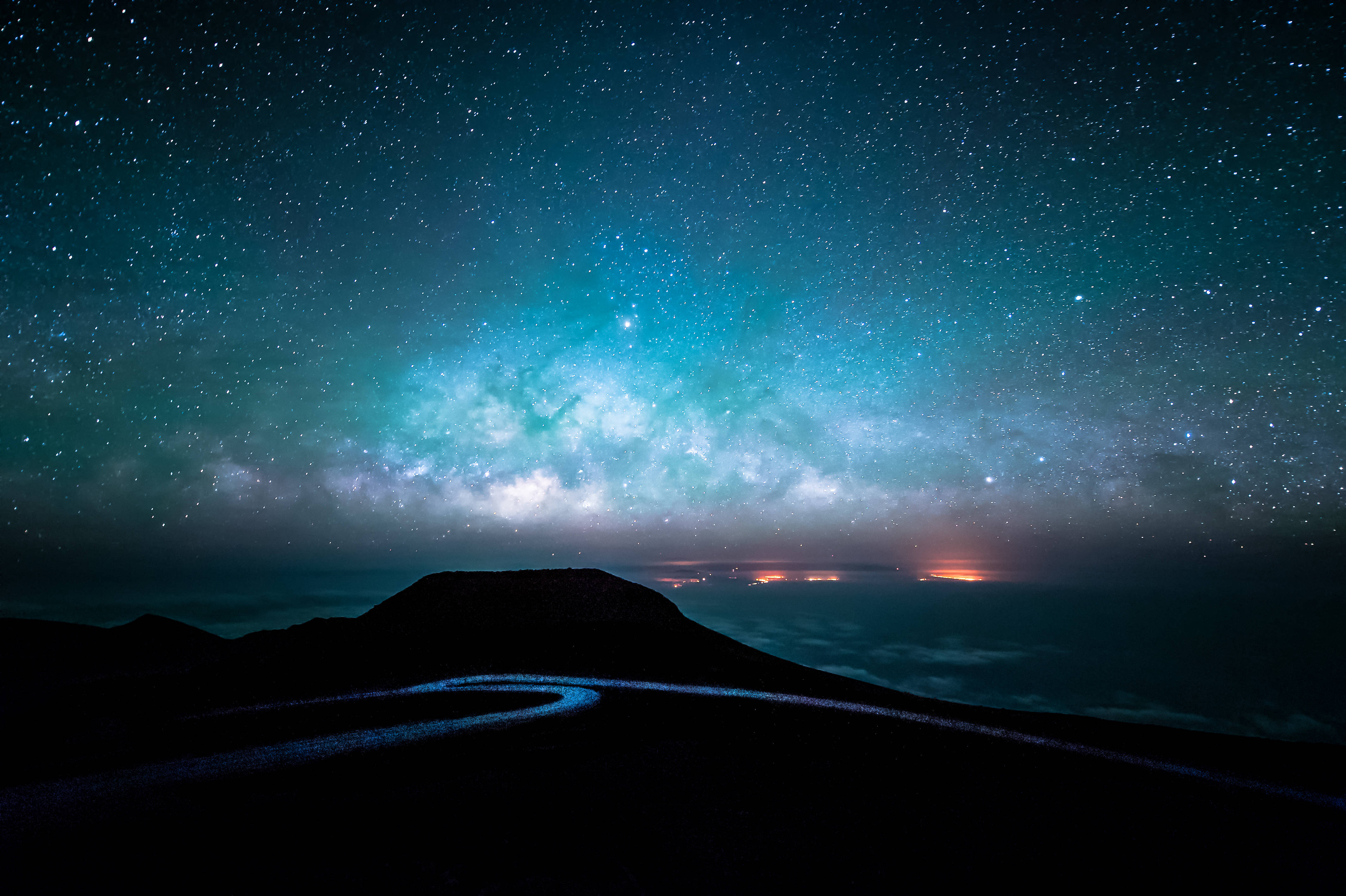Starry Sky 桌布 壁紙 — 一條蜿蜒的道路在黑暗的山脈中穿行，上方是充滿活力的藍綠色星空，閃耀的銀河發出光芒。