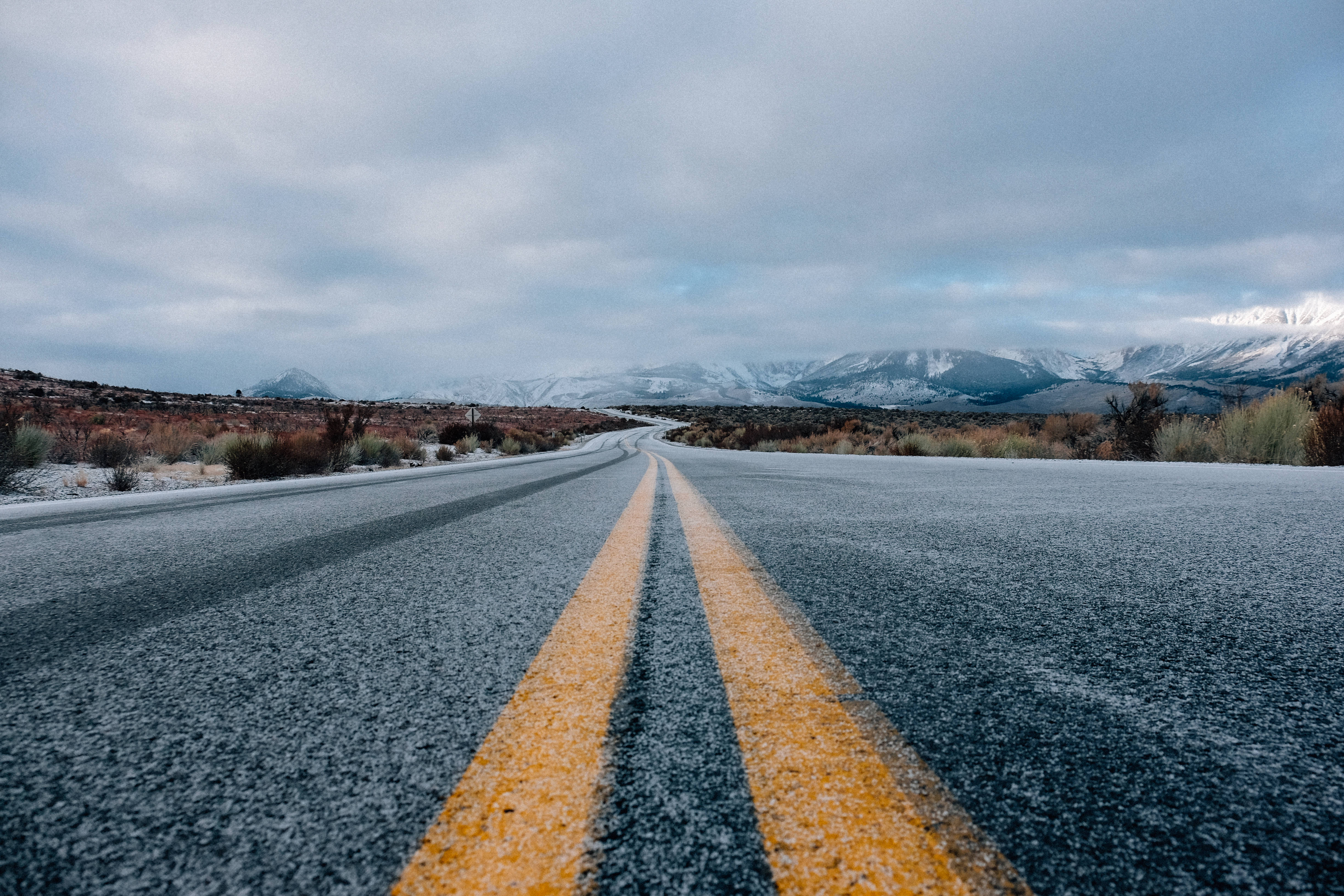 Road 桌布 壁紙 — 一條蜿蜒的道路帶有黃色線條，在陰沉的冬日天空下延伸向積雪的山峰。