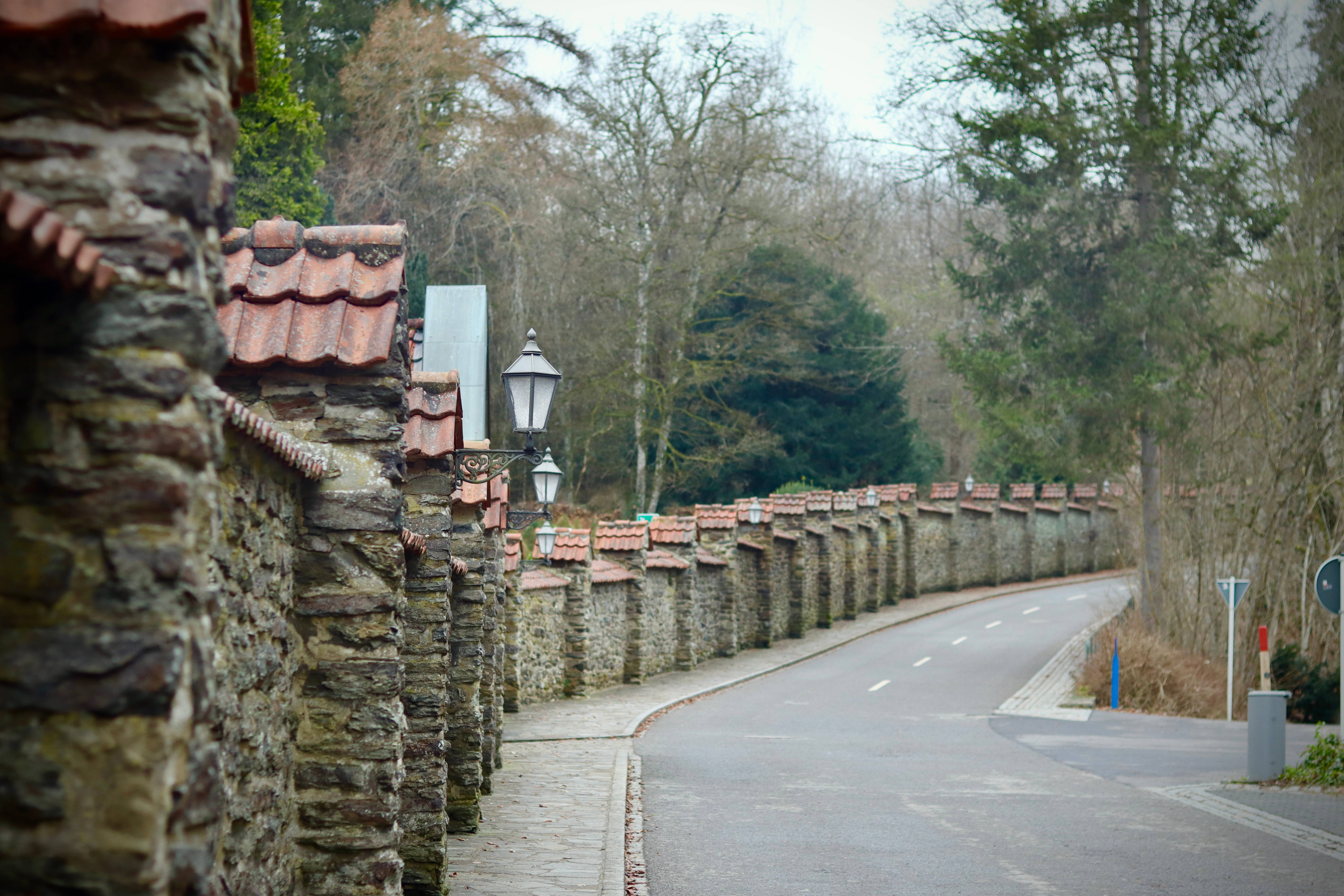 Luxembourg 桌布 壁紙 — 一條蜿蜒的道路沿著一條長長的石牆蜿蜒而過，石牆頂部鋪著紅瓦，天空陰沉。