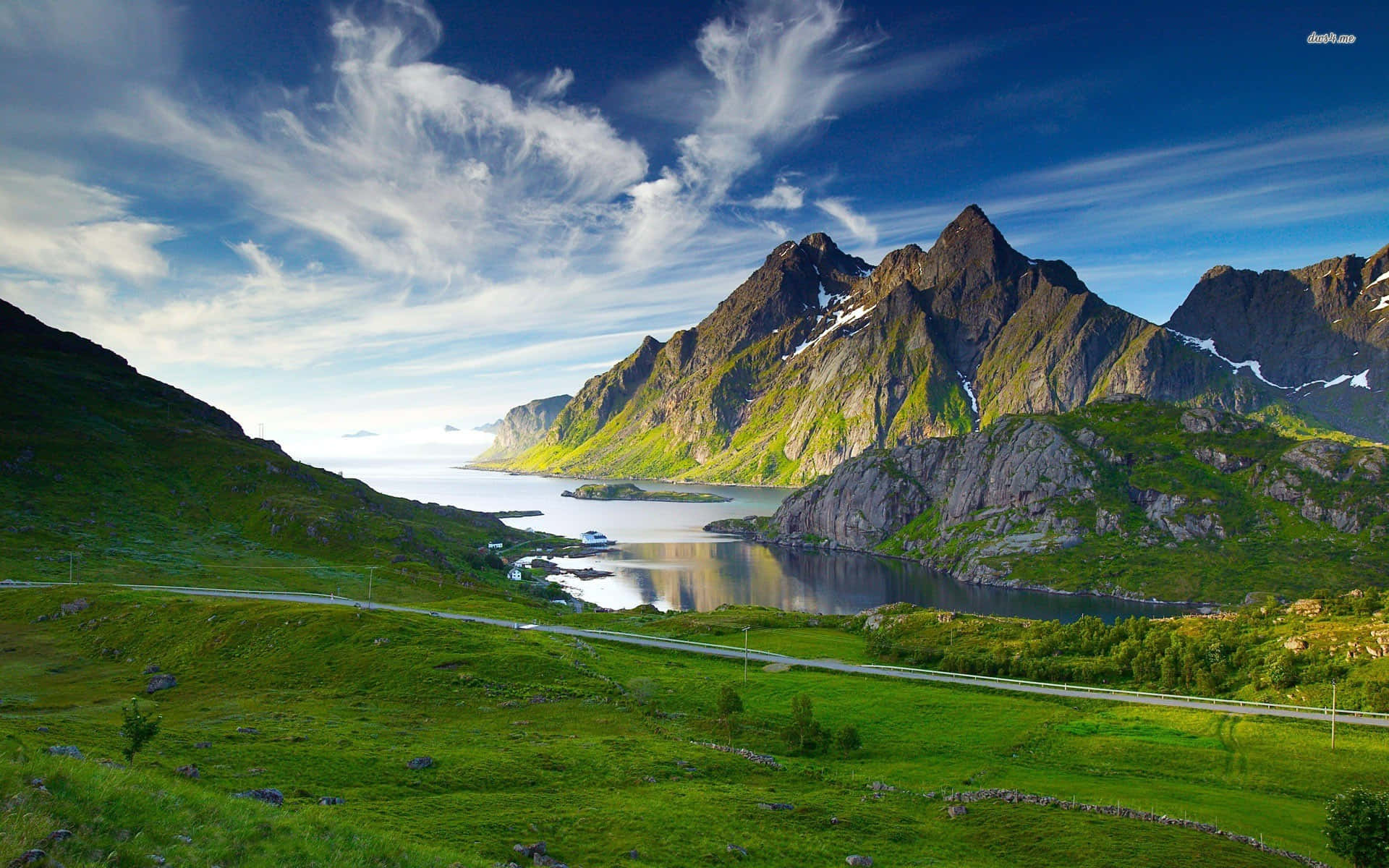 Mountain Scenery 桌布 壁紙 — 一條蜿蜒的道路環繞著充滿活力的綠色山丘，通往一個寧靜的峽灣，兩旁是崎嶇的積雪山脈，上方是明亮的藍天，點綴著縷縷白雲。