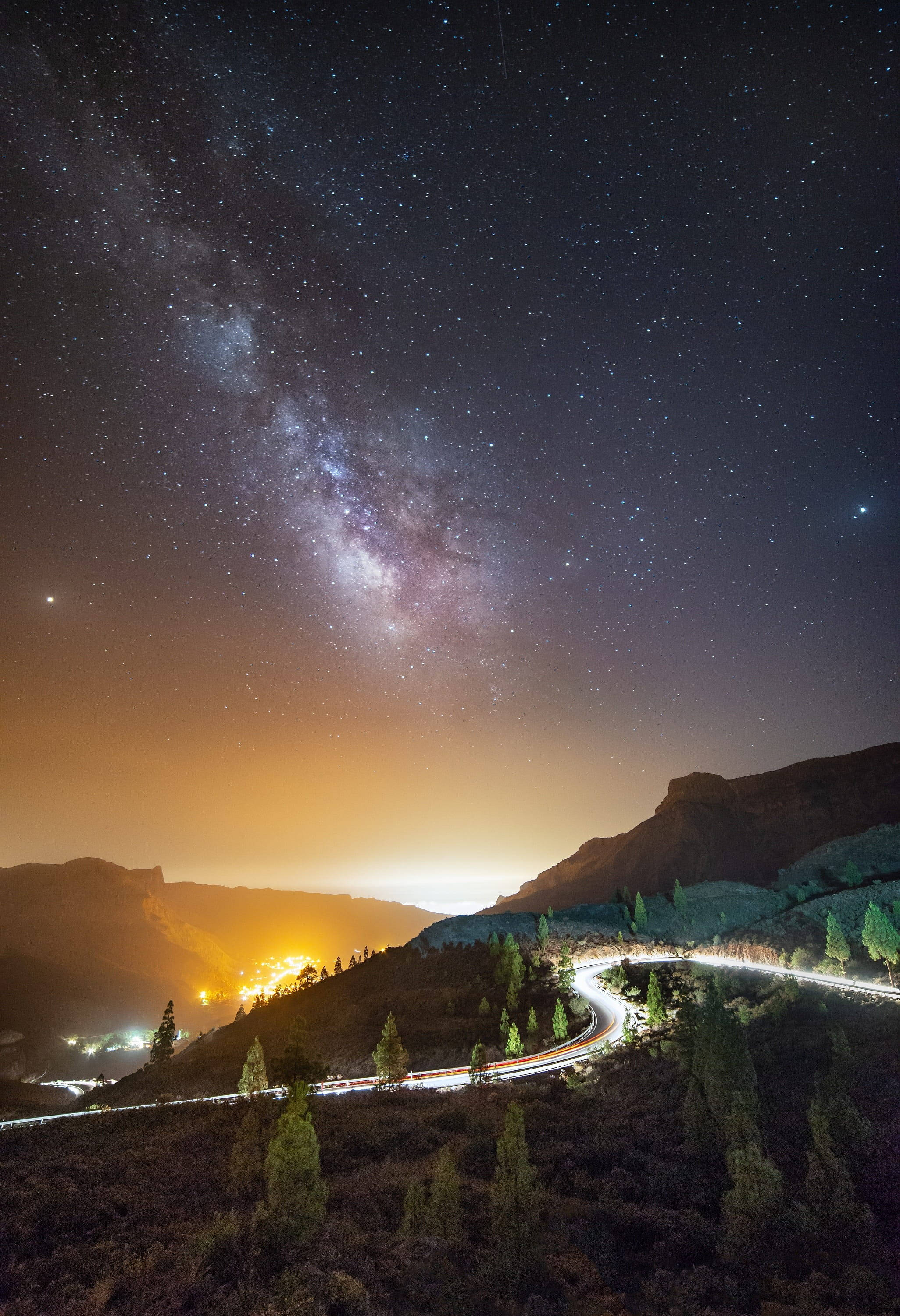 Road 桌布 壁紙 — 一條蜿蜒的道路穿過山區景觀，上方是充滿活力的星空，銀河在頭頂閃耀。