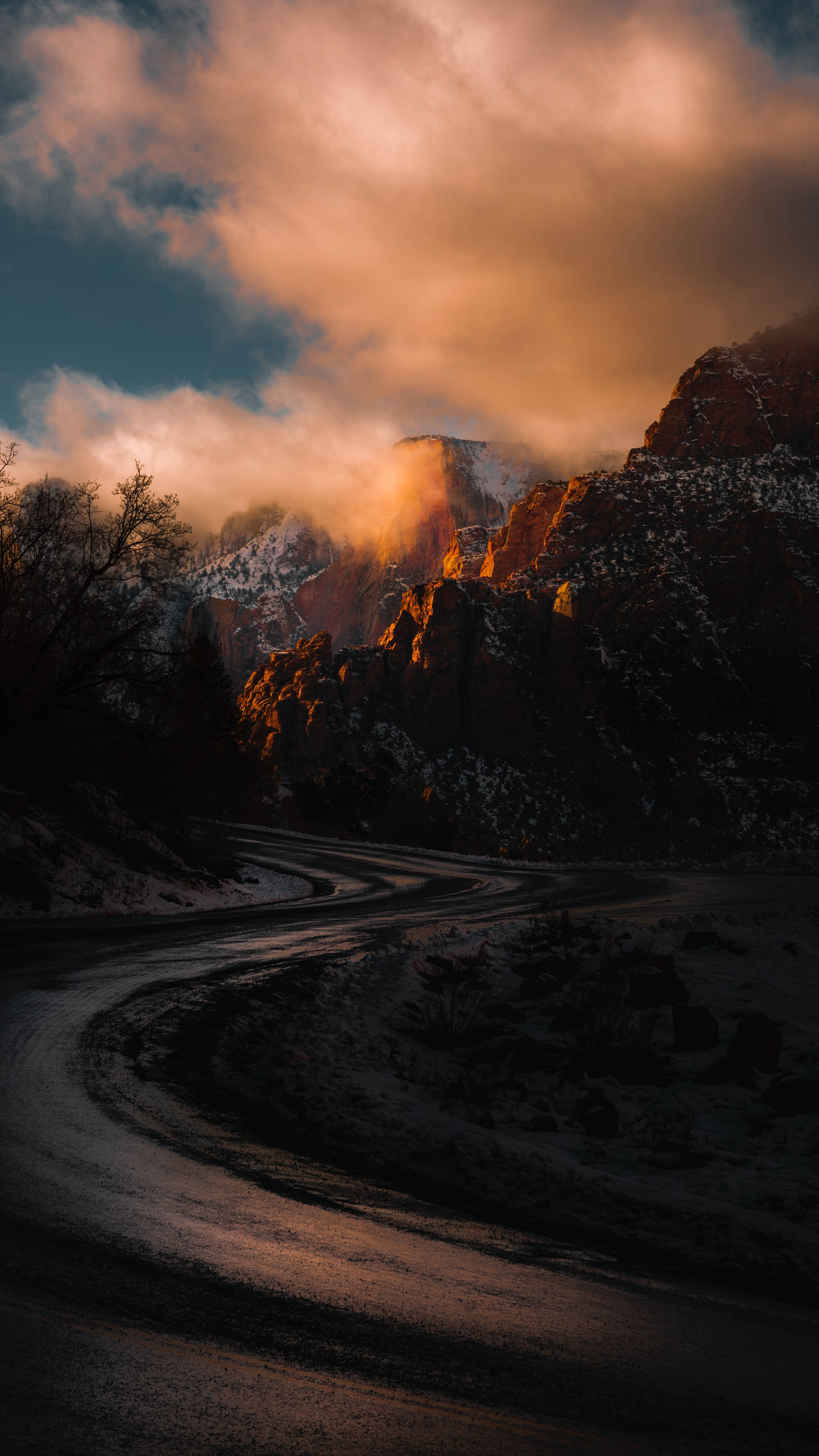 Road 桌布 壁紙 — 一條蜿蜒的道路穿過積雪的山脈，金色的夕陽光線穿過雲層，照耀在崎嶇的山峰上。