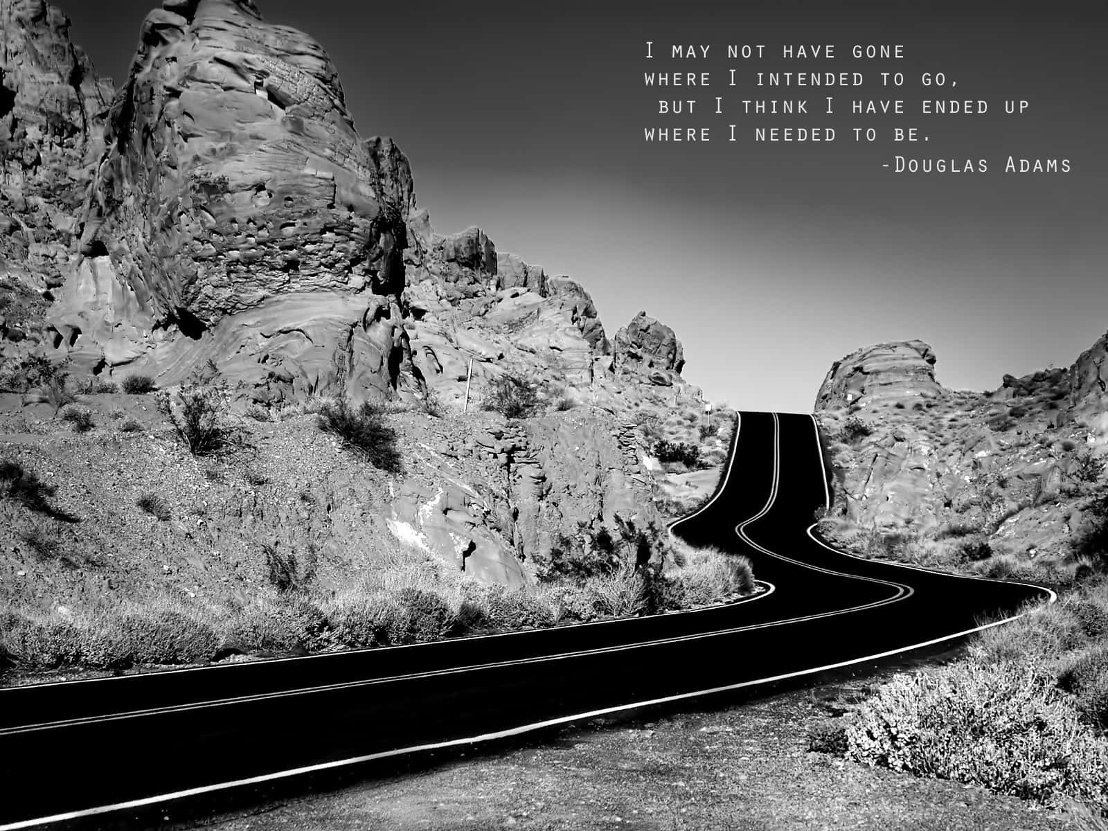 Positive Quotes 桌布 壁紙 — 一條蜿蜒的道路穿過荒涼的岩石地形，廣闊的天空上疊加了道格拉斯·亞當斯的名言。