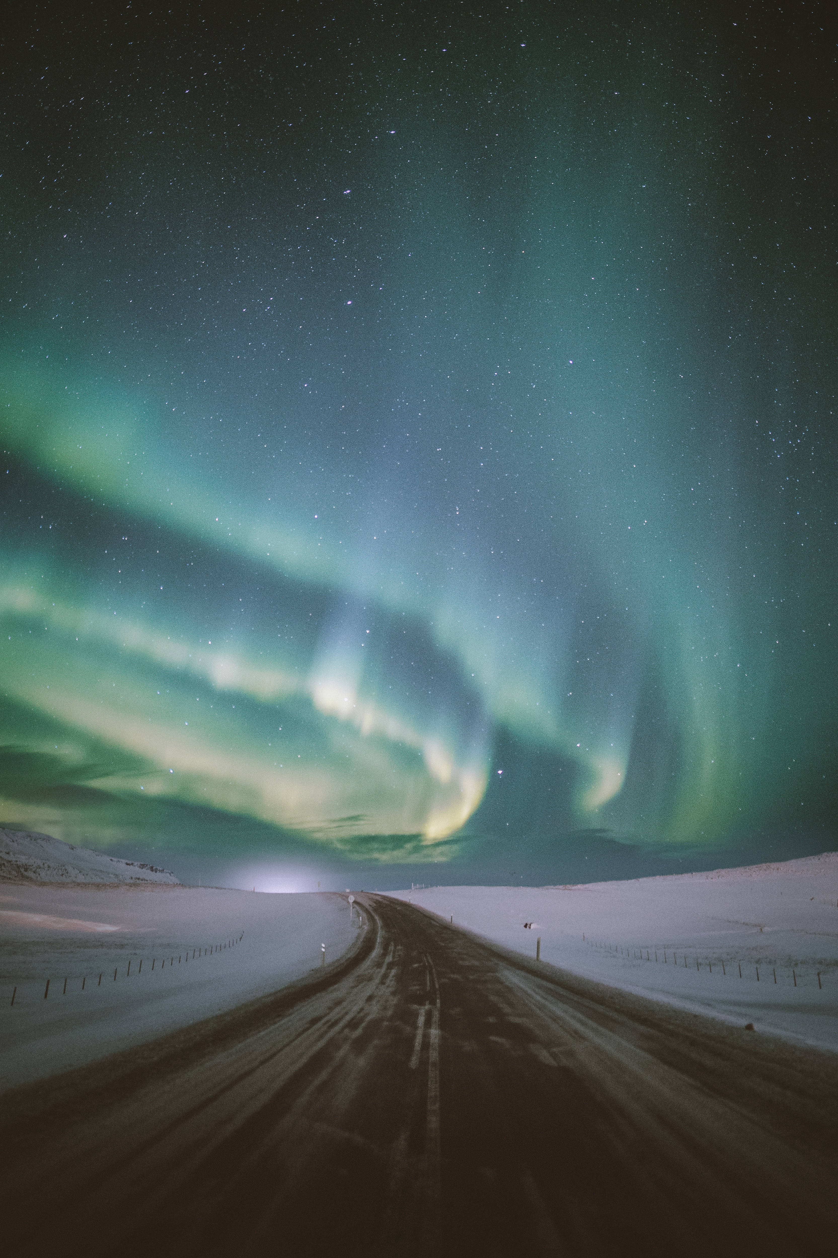 lights 桌布 壁紙 — 一條蜿蜒的道路穿過雪原，在充滿活力的綠色北極光在星空夜空中舞動之下。