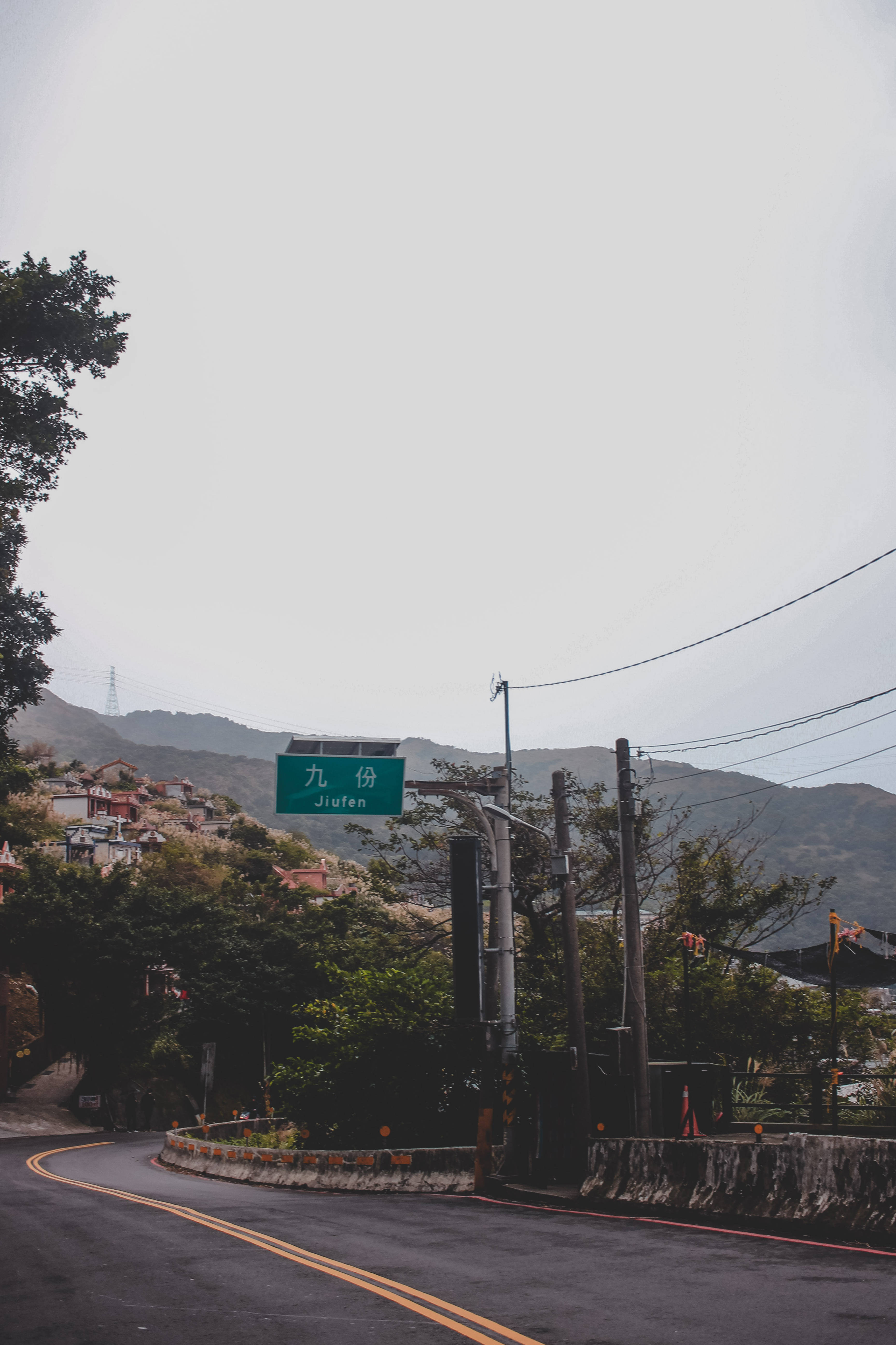 Lockscreen 桌布 壁紙 — 一條蜿蜒的道路穿過霧氣瀰漫的山村，瀝青路面上方懸掛著一個綠色的 Jiafen 標誌。