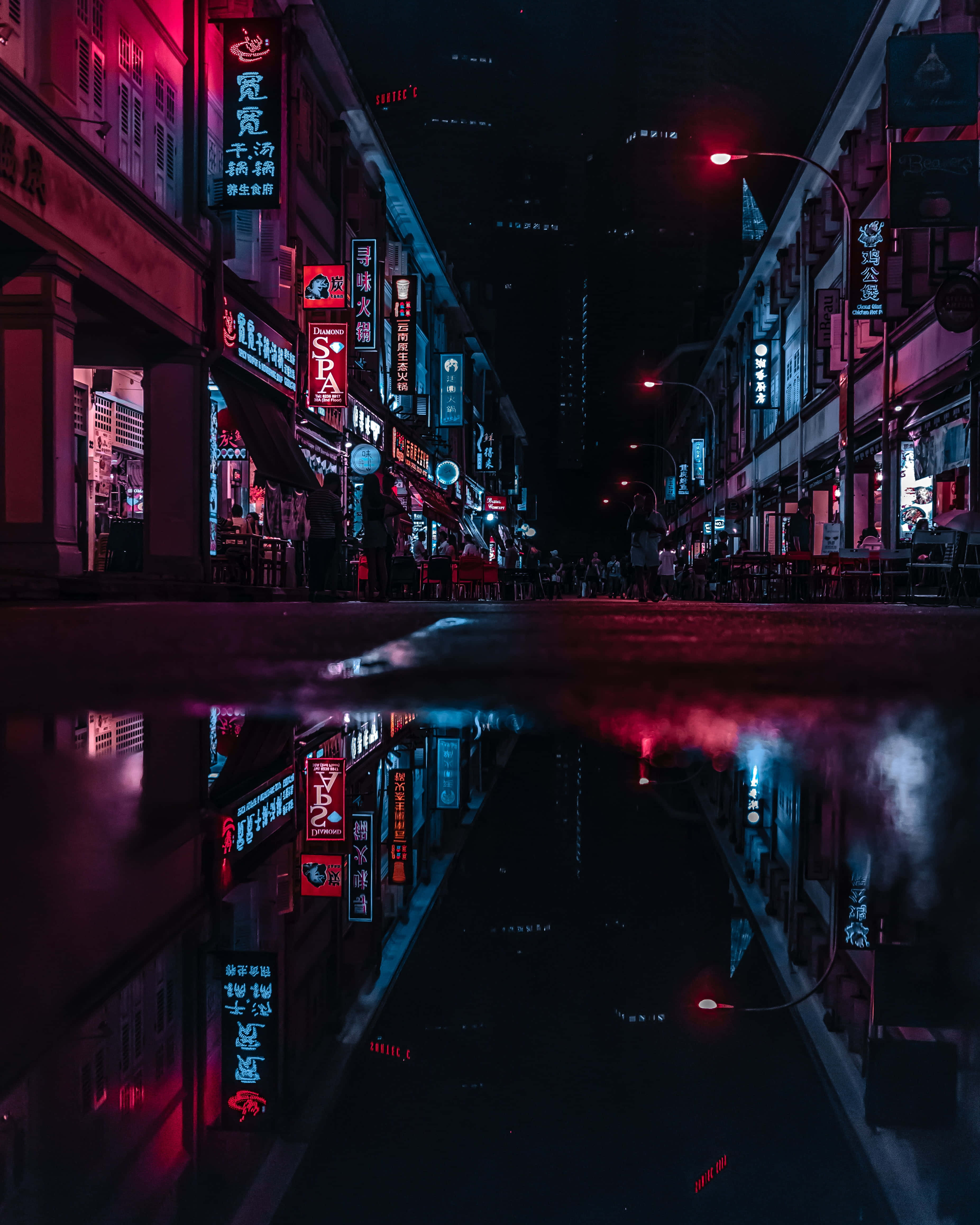 Street 桌布 壁紙 — 一條被雨水打濕的都市街道在夜晚反射著周圍建築物的霓虹招牌和發光的燈光。