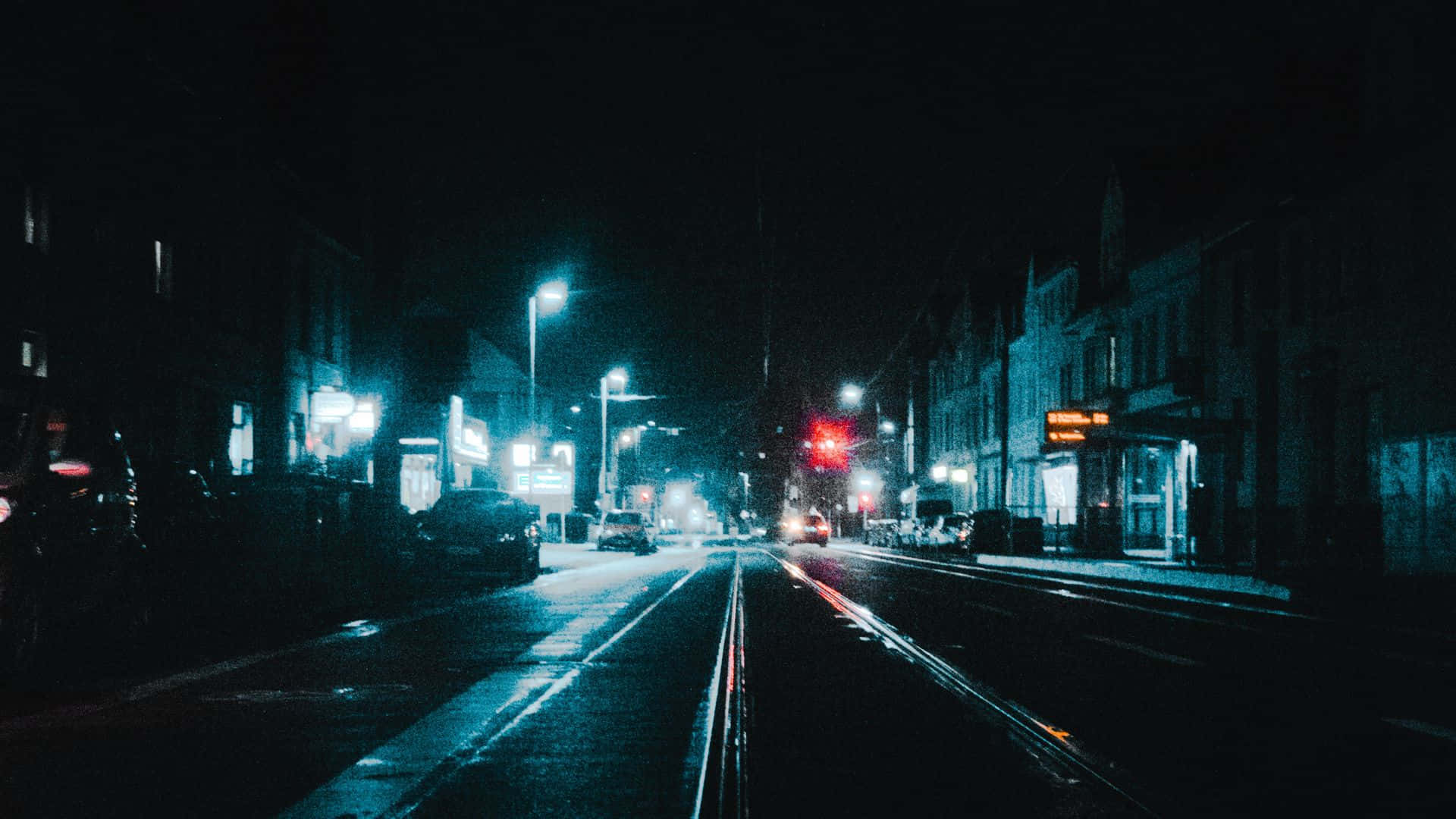Dark Crossroad 桌布 壁紙 — 一條被雨水打濕的都市街道在夜晚閃爍著霓虹燈光，在街燈下反射在濕漉漉的路面上。