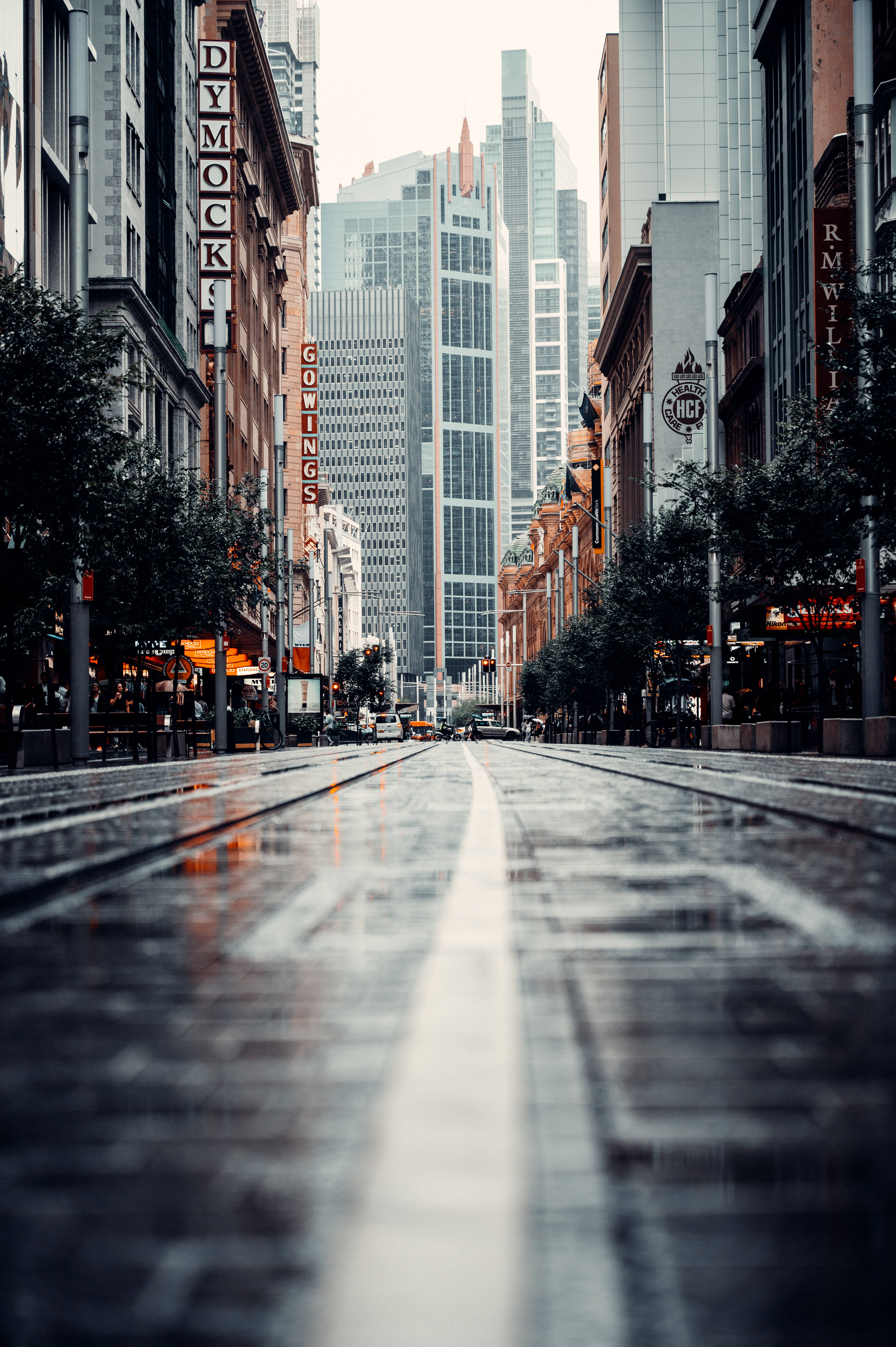 城市 桌布 壁紙 — 一條被雨水浸濕的都市街道，有電車軌道，在陰天天空下反射著霓虹燈牌和高聳的摩天大樓。