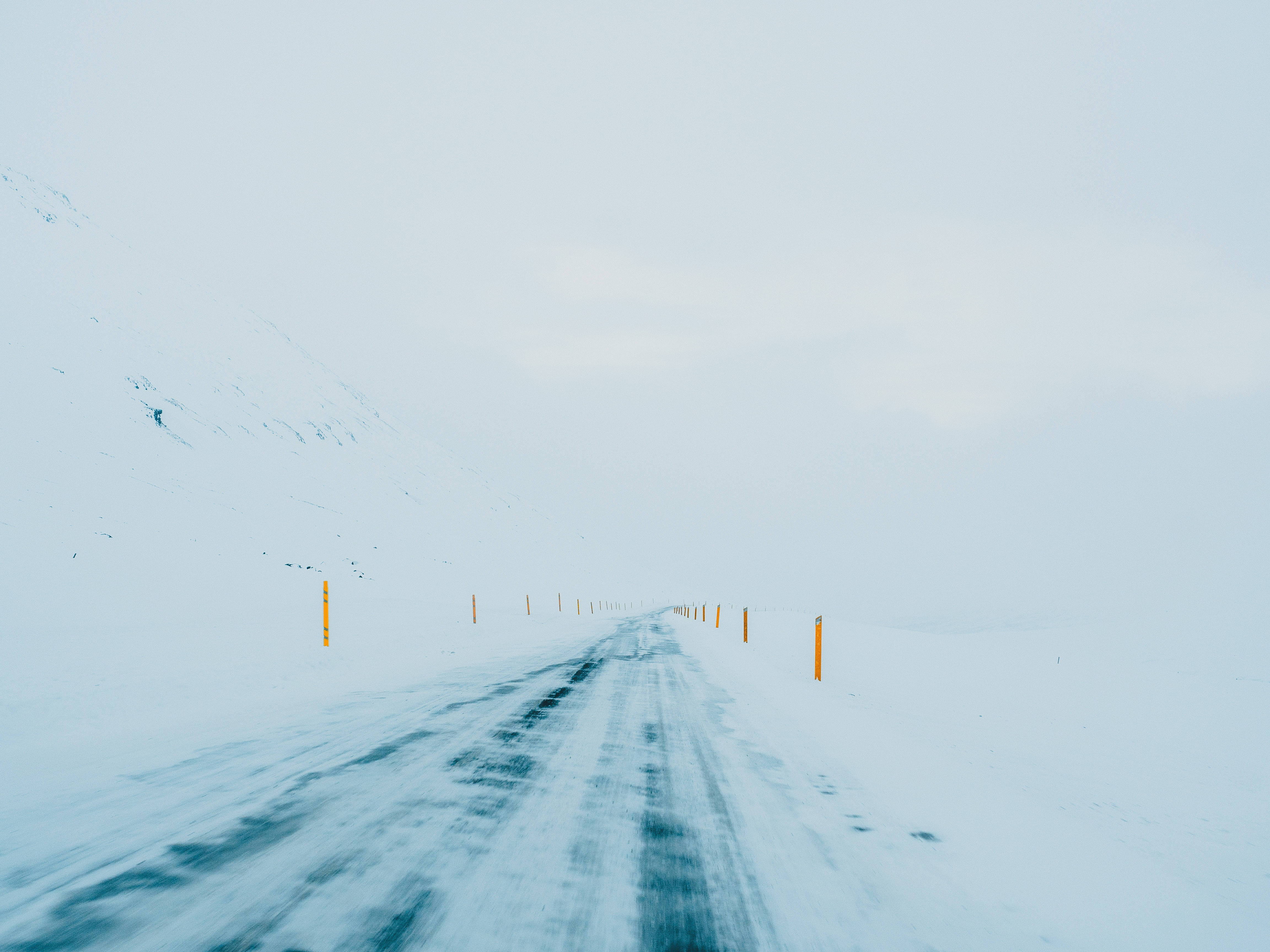 桌布 壁紙 — 一條被雪覆蓋的道路延伸至一片朦朧的白色冬季景觀，以橙色柱子標記。
