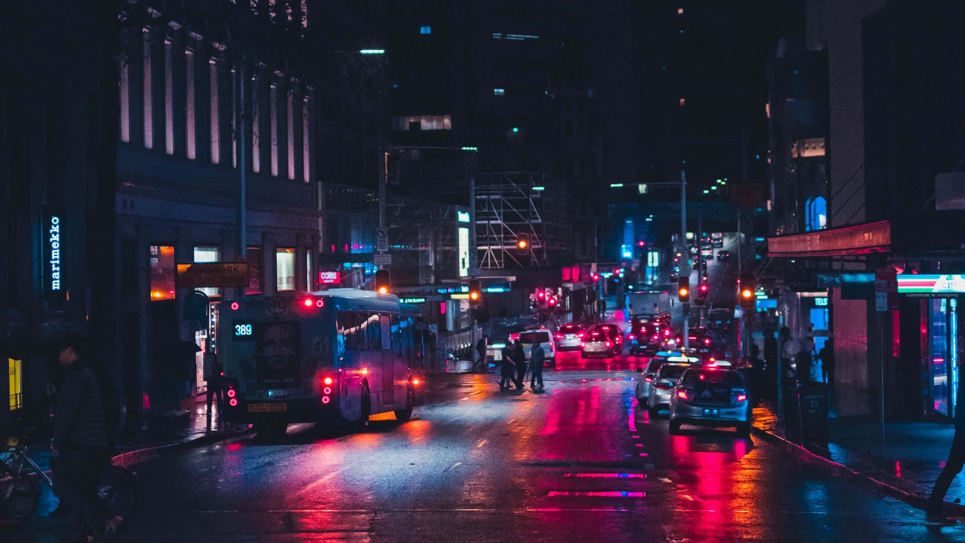 夜景城市 桌布 壁紙 — 一條被霓虹燈浸染的夜晚城市街道，在潮濕的路面上反射出鮮豔的紅色和藍色燈光，汽車和巴士在城市場景中穿梭。