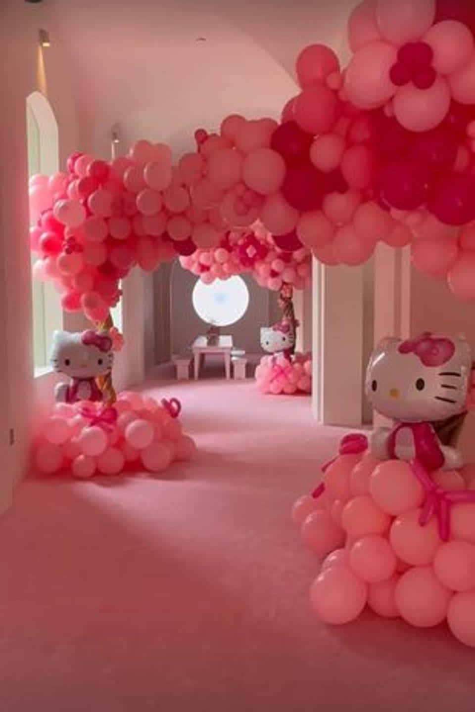 Hello Kitty Party 桌布 壁紙 — 一條走廊裝飾著粉紅色和紅色的氣球拱門以及Hello Kitty公仔，營造出夢幻的慶祝氣氛。