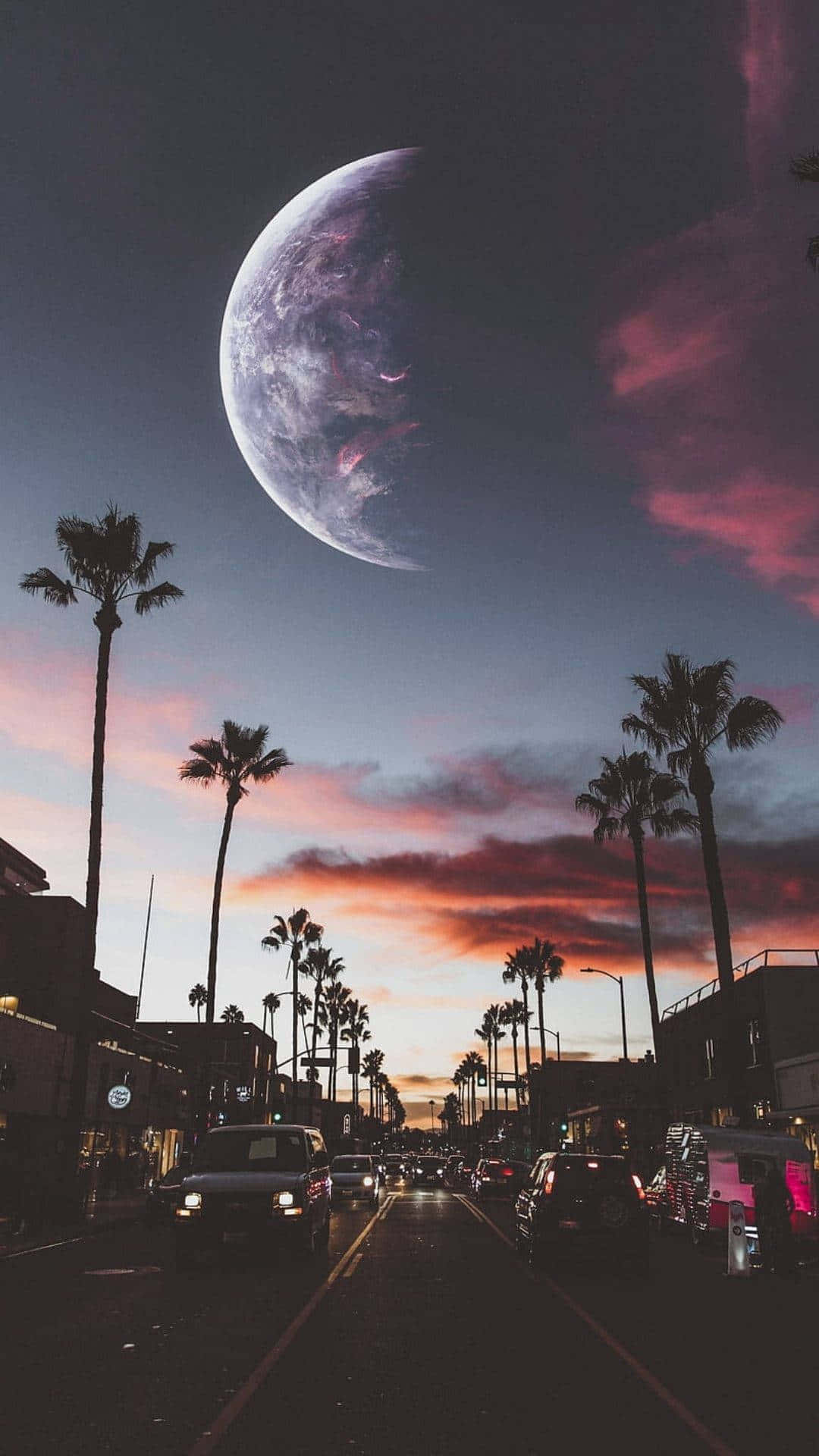 桌布 壁紙 — 一條超現實的城市街道，兩旁種滿棕櫚樹，上方掛著巨大的新月和充滿活力的粉橙色日落天空。