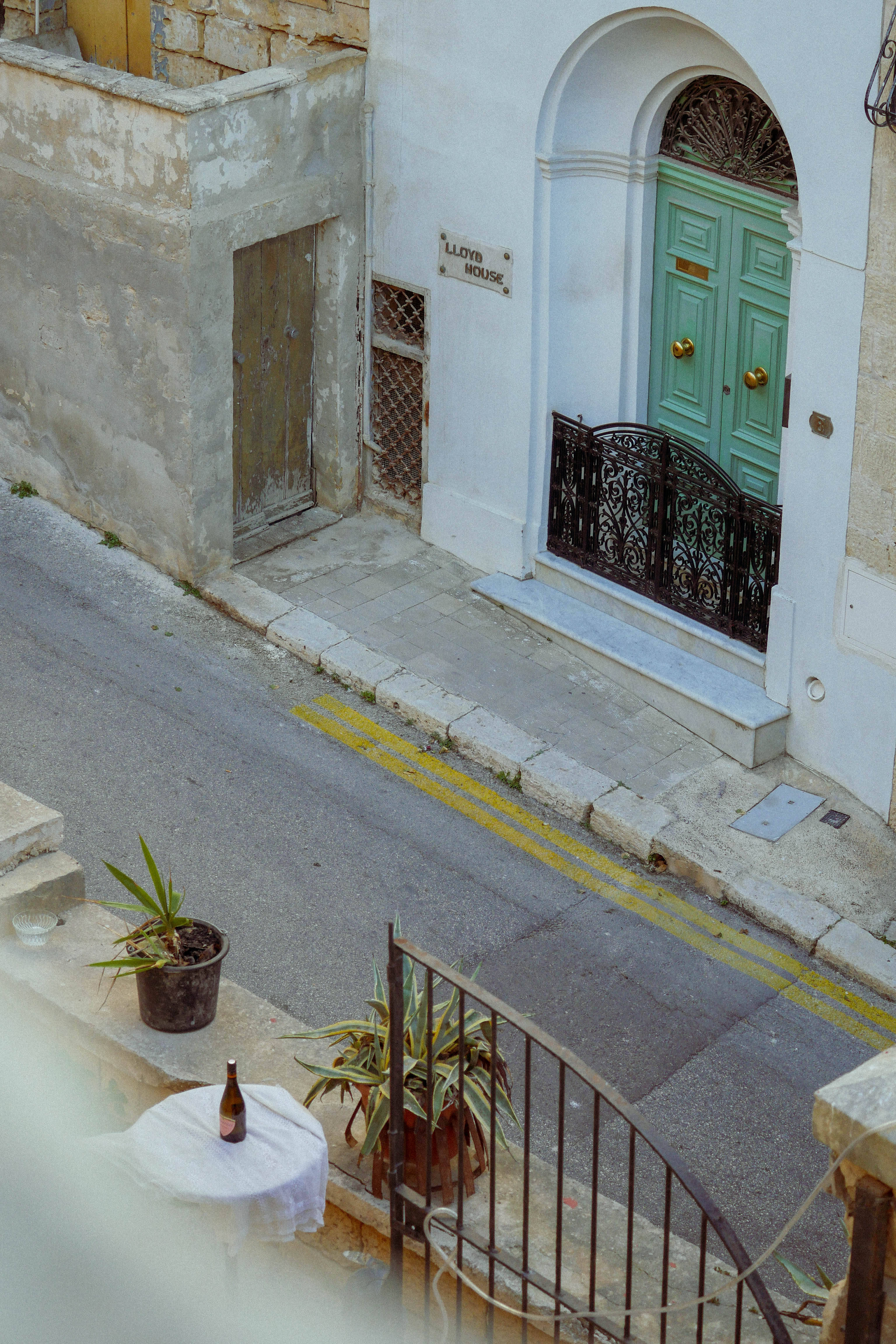 Malta 桌布 壁紙 — 一條迷人的狹窄街道，有一扇充滿活力的綠色門和石陽台上的盆栽植物，俯瞰著一條寧靜的小巷。
