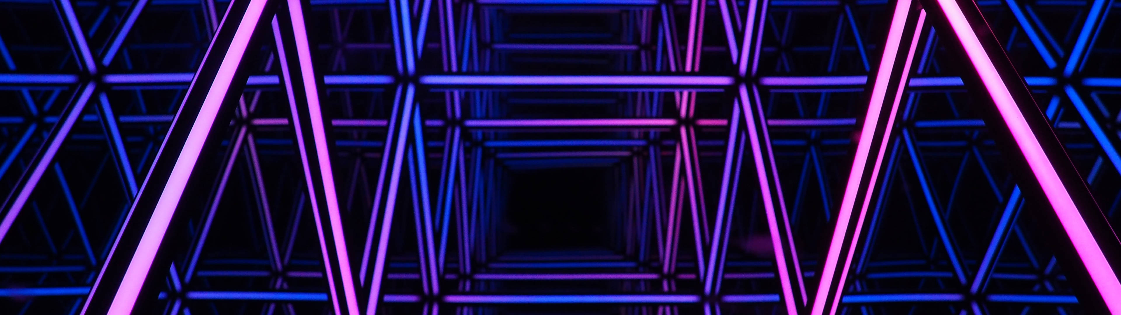 lights 桌布 壁紙 — 一條迷人的霓虹隧道，由發光的粉紅色和藍色幾何條紋組成，逐漸消失在黑暗中。