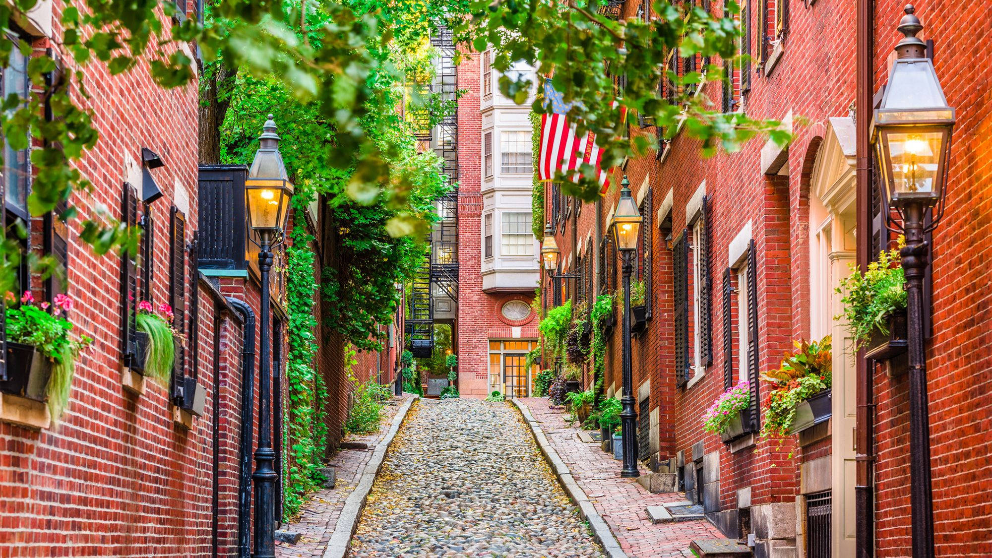 Boston 桌布 壁紙 — 一條迷人的鵝卵石小巷，兩旁是紅磚建築，掛著花籃和發光的燈籠。
